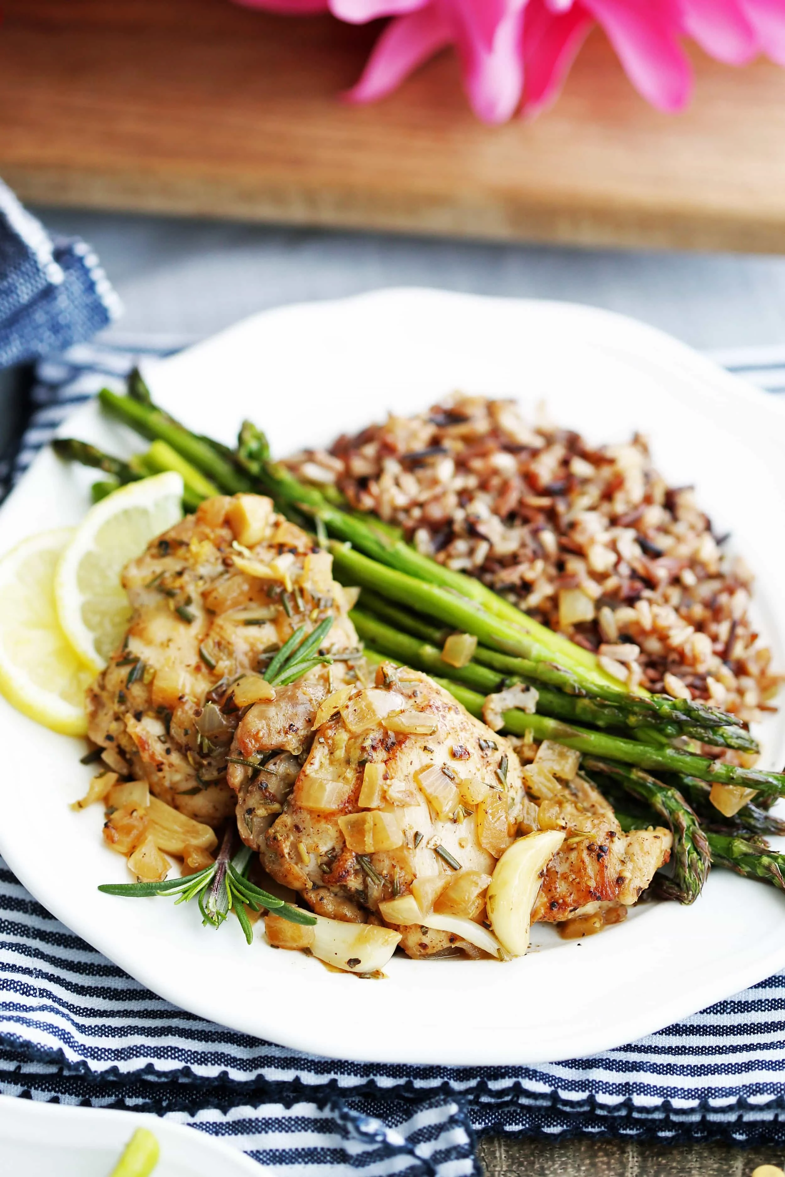 Two rosemary garlic chicken thighs, roasted asparagus, and wild rice on a white plate.