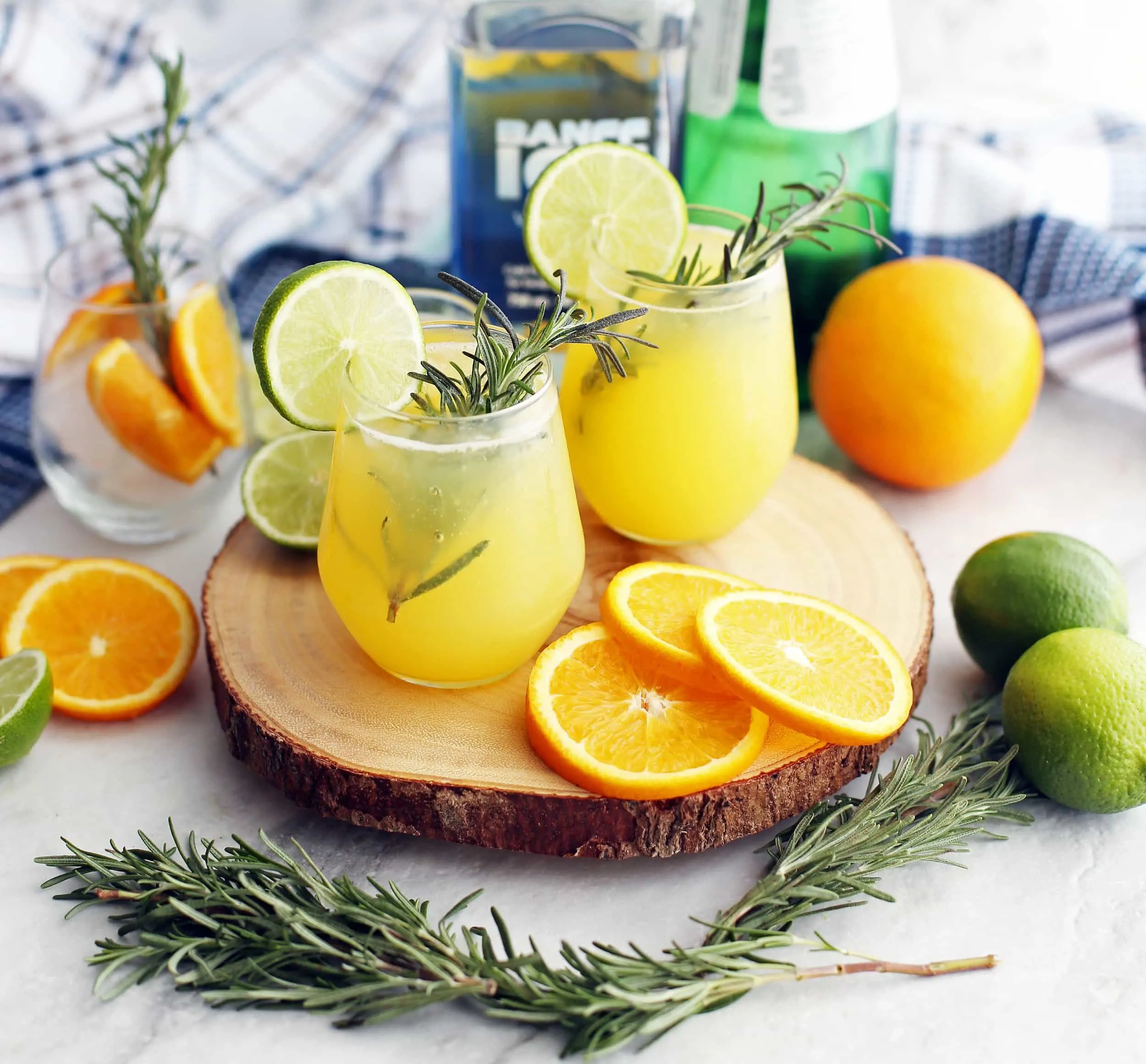 A side view of two glasses of sparkling maple orange vodka with fresh rosemary sprigs, lime slices,and orange slices.