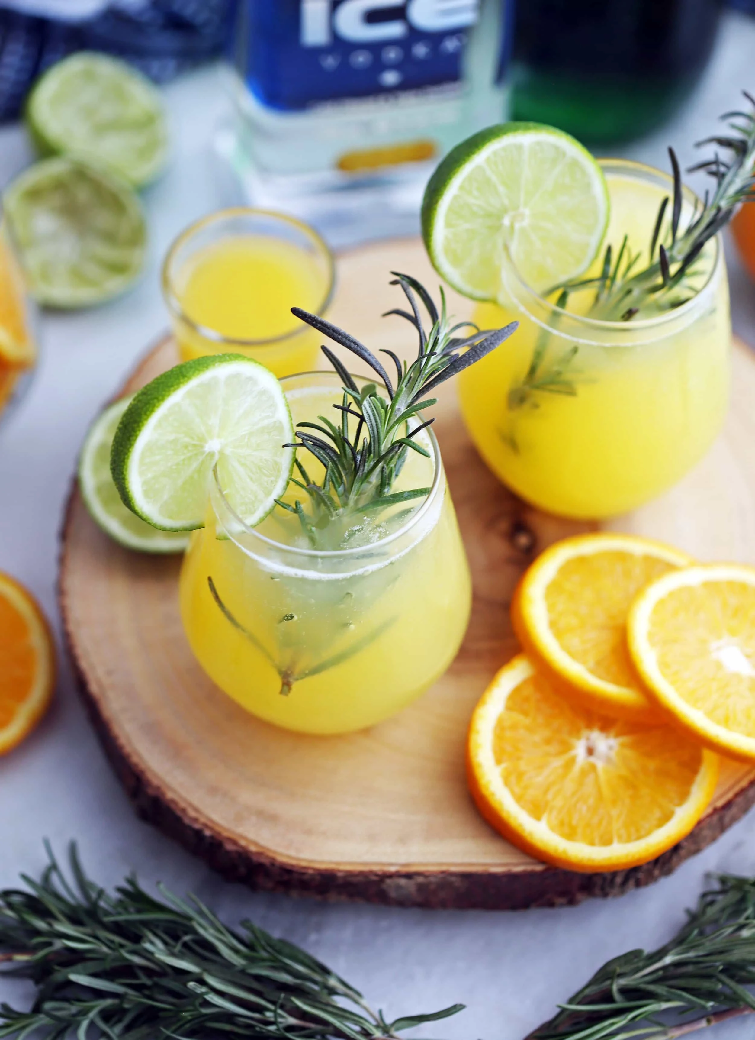 An high-angled view of two glasses of sparkling maple orange vodka with fresh rosemary sprigs, lime slices,and orange slices.