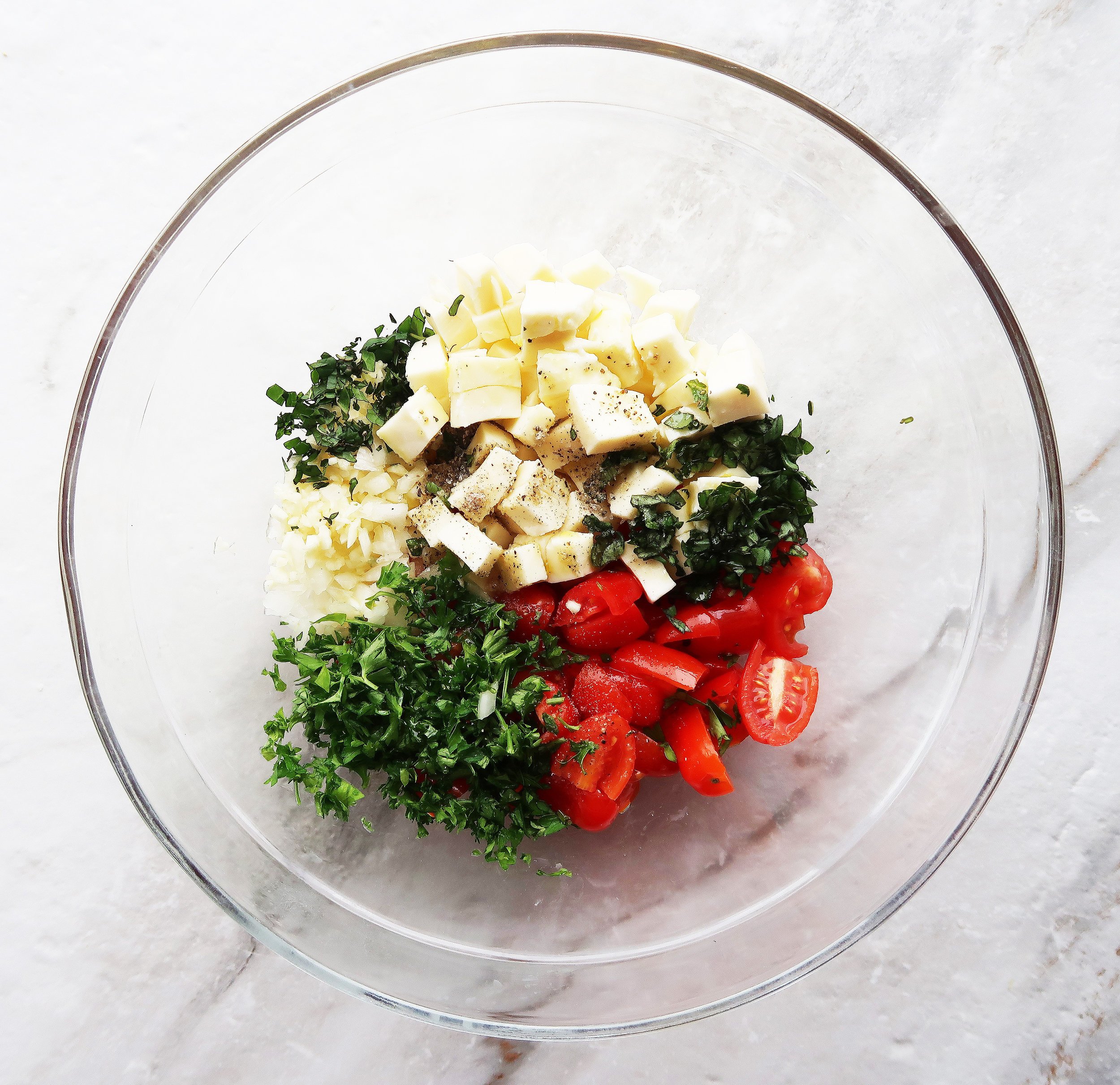 A bowl of quinoa with tomatoes, mozzarella, and herbs.