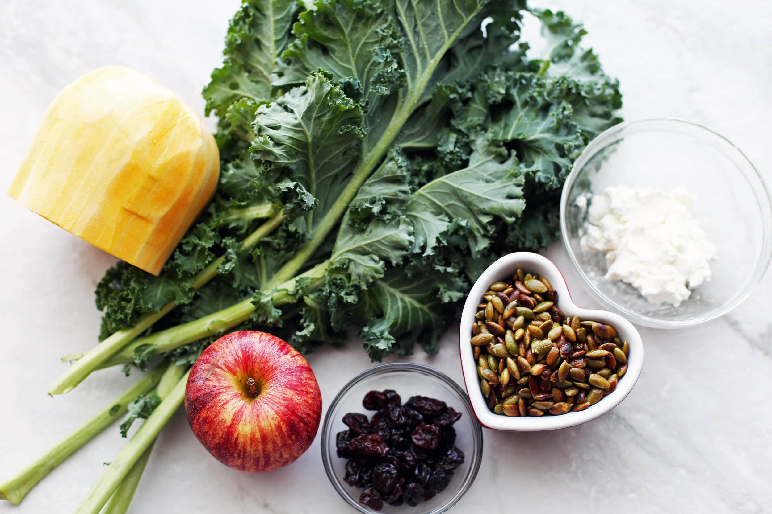 Overhead view of kale, apple, butternut squash, pumpkin seeds, and goat cheese.