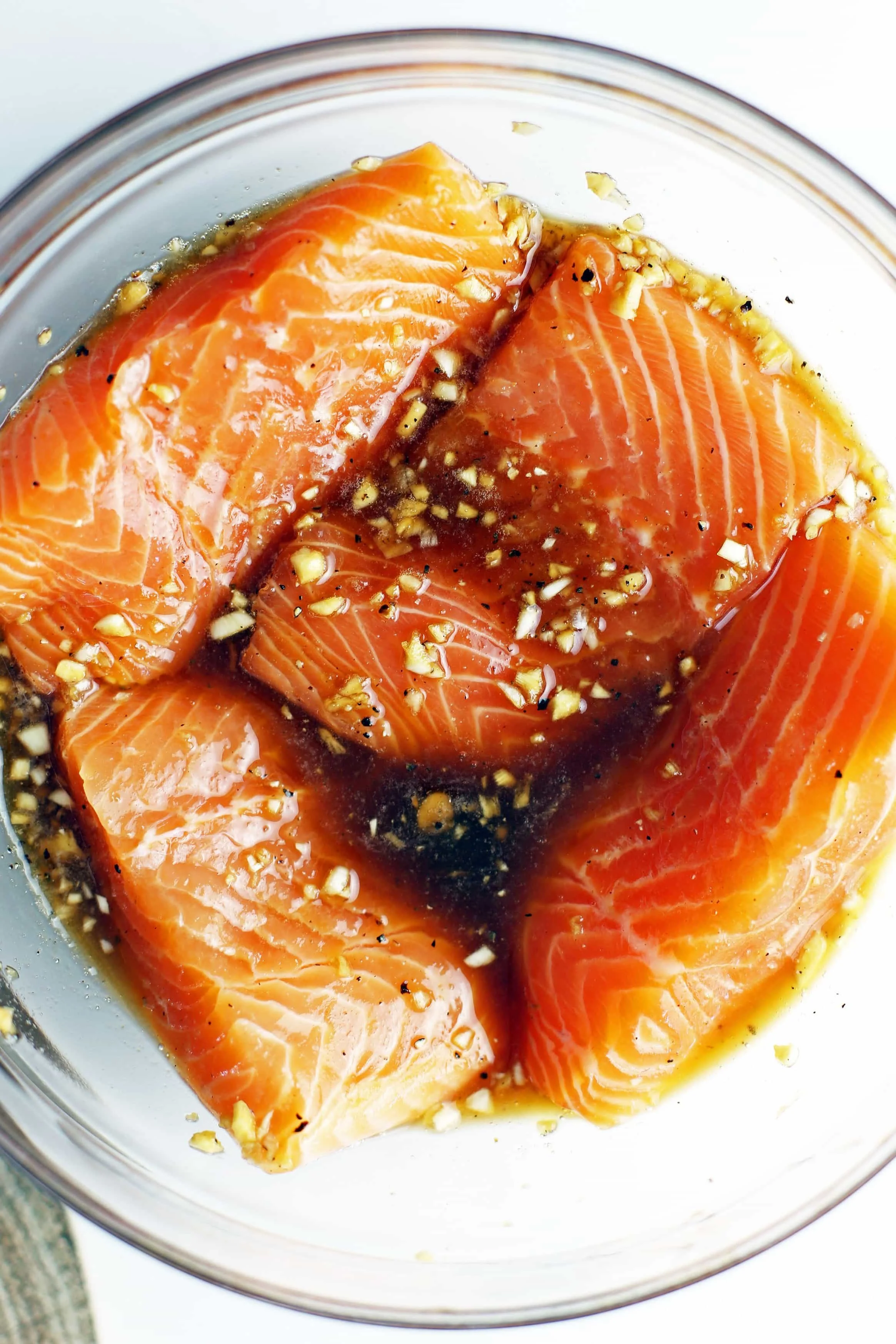 Four skinless salmon fillets covered in honey garlic marinade in a large glass bowl.