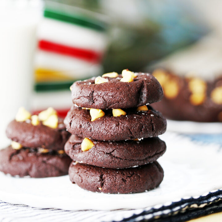 Four Salted Chocolate Butterscotch Chip Cookies stacked on a white plate with a glass of milk beside it.