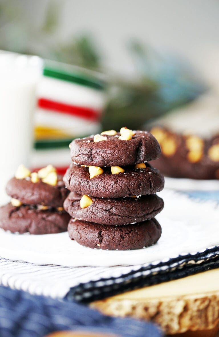 Four Salted Chocolate Butterscotch Chip Cookies stacked on a white plate with a glass of milk beside it.