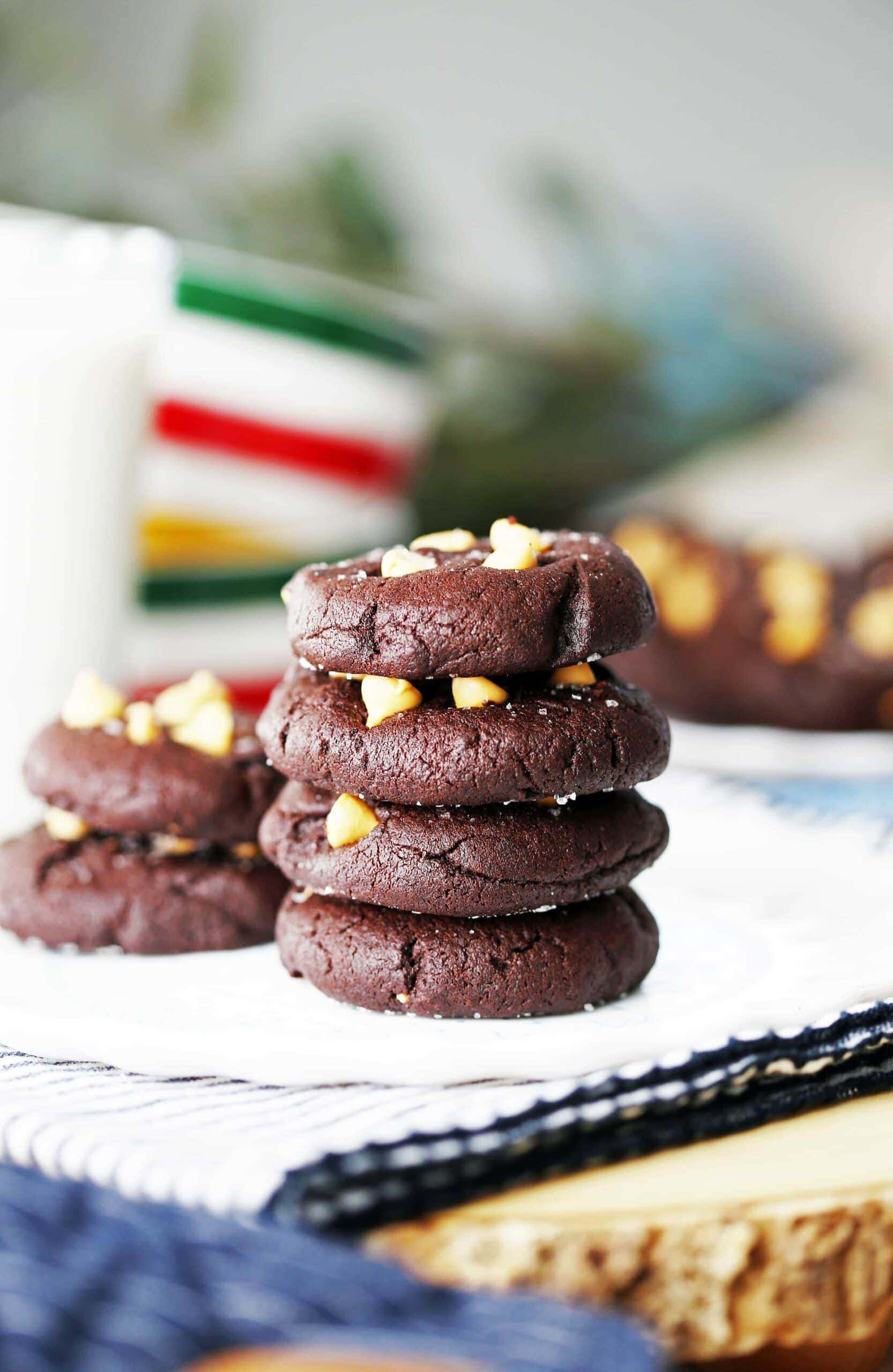 Four Salted Chocolate Butterscotch Chip Cookies stacked on a white plate with a glass of milk beside it.