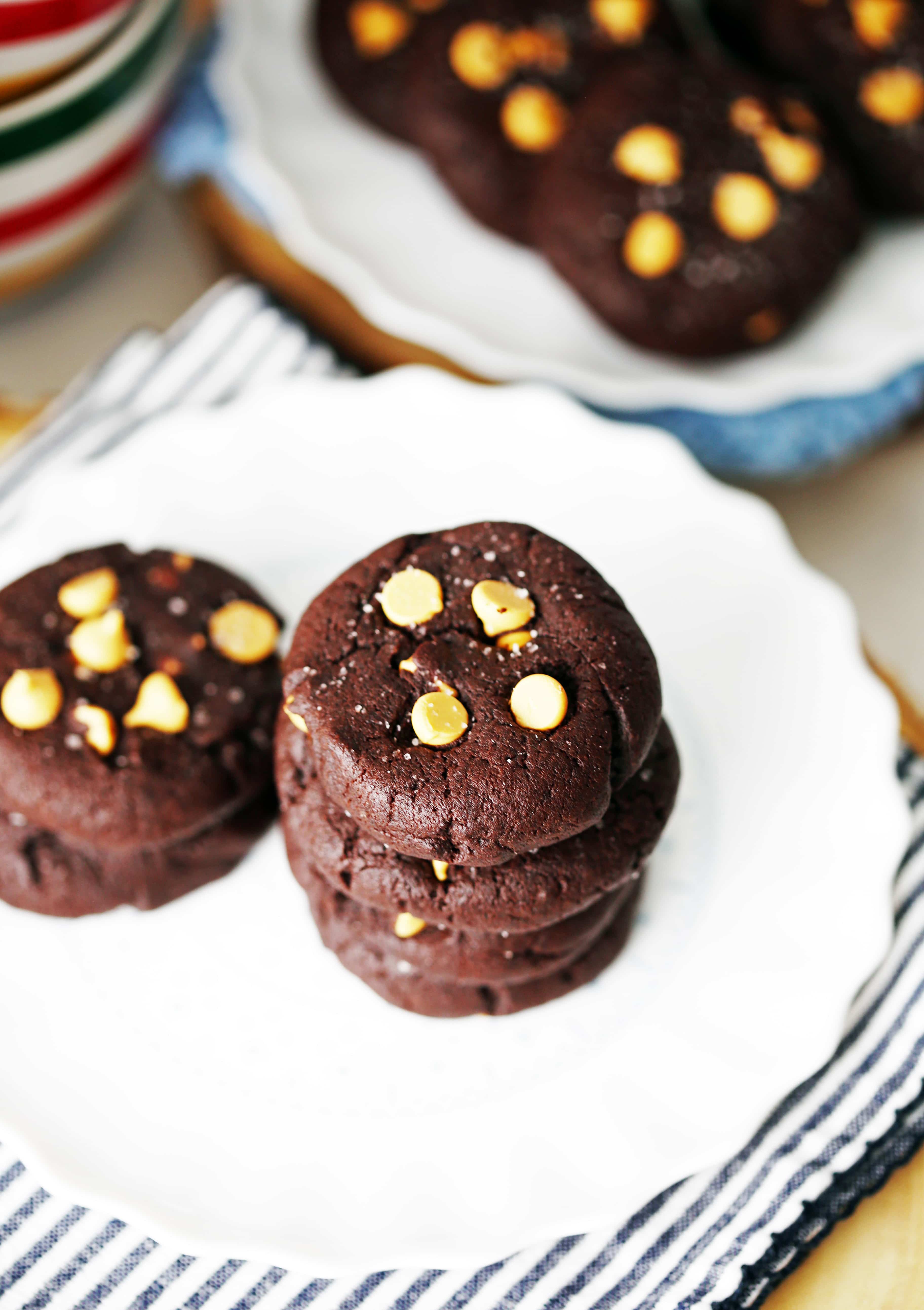 An angled overhead view of chocolate butterscotch chip cookies on two white plates.