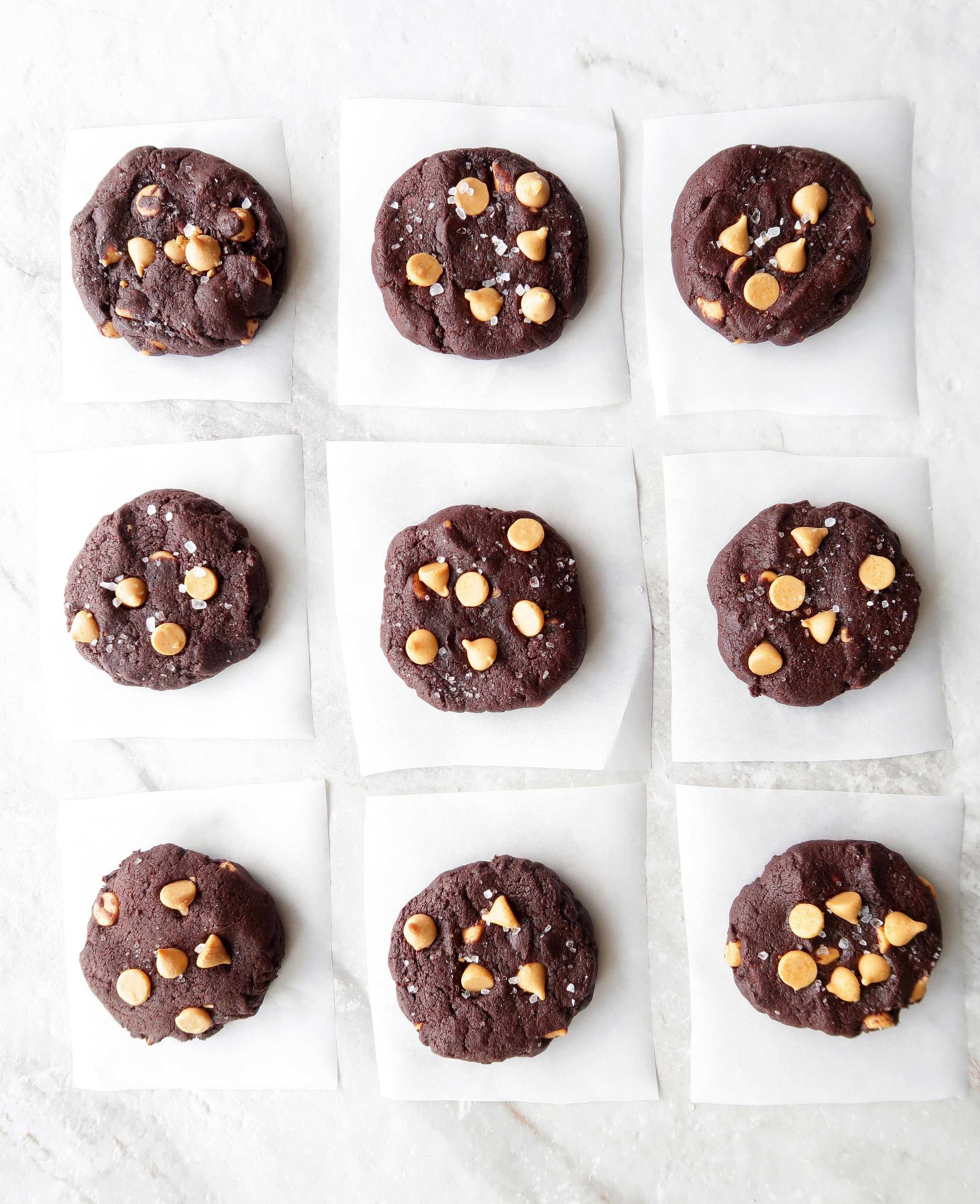 Nine baked salted chocolate butterscotch chip cookies in rows of three on a white marble surface.