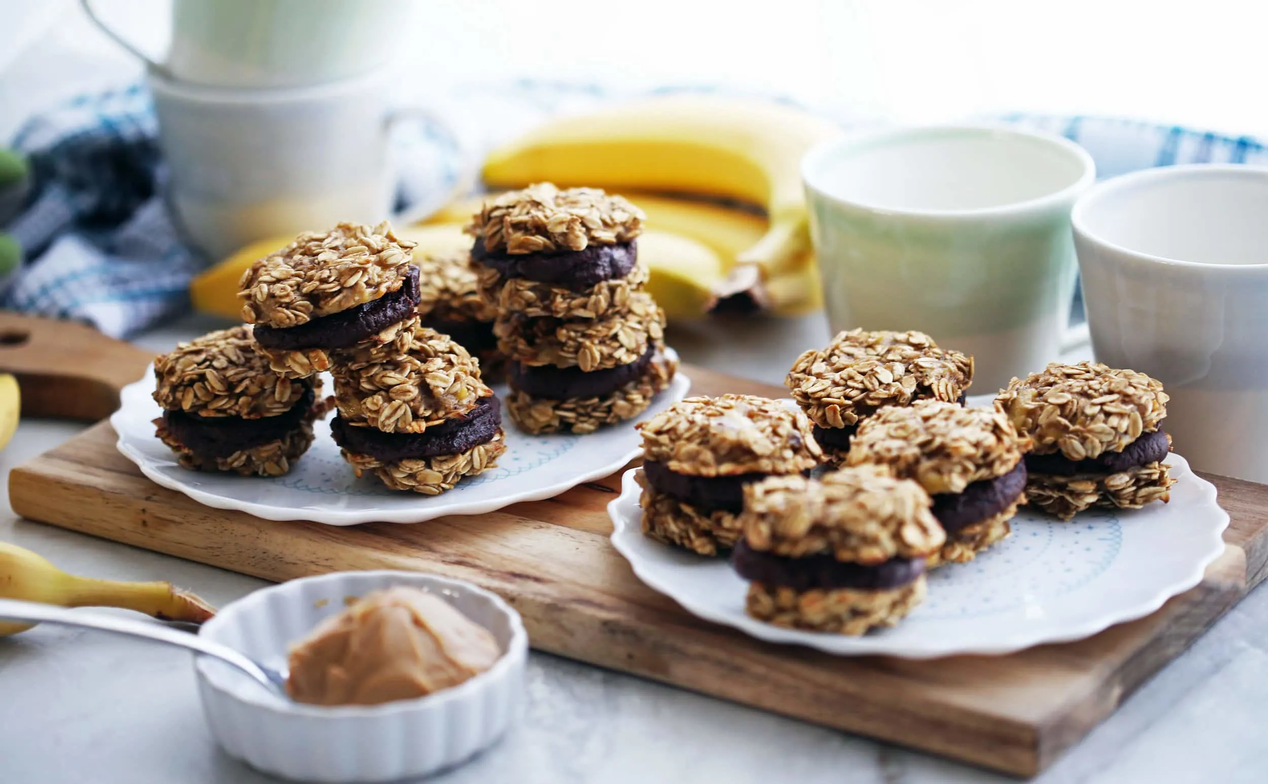 Two plates on a wooden board full of banana oatmeal sandwich cookies with peanut butter cocoa filling.