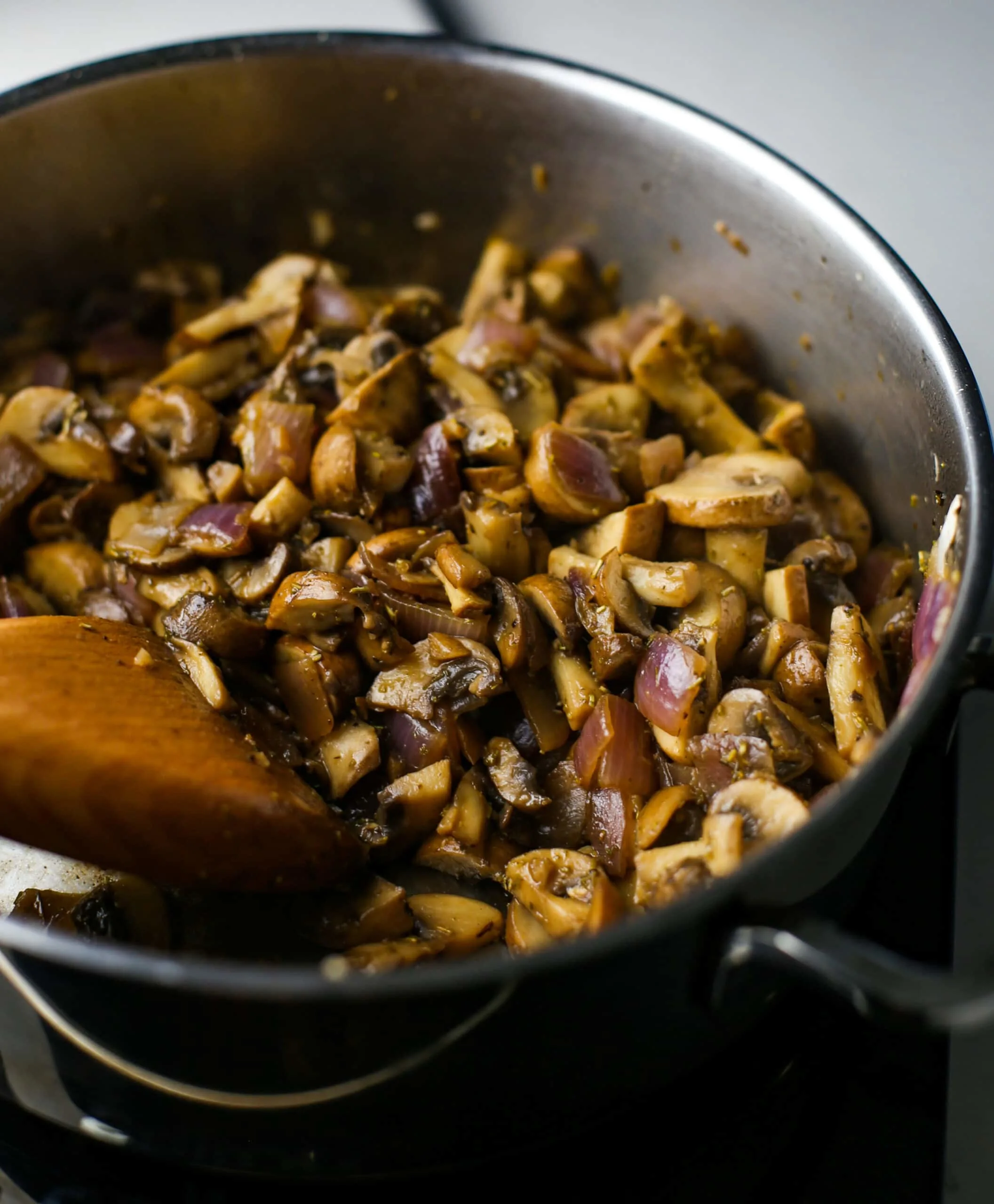 Sauteed browned sliced cremini mushrooms and red onions in a stainless steel saucepan.