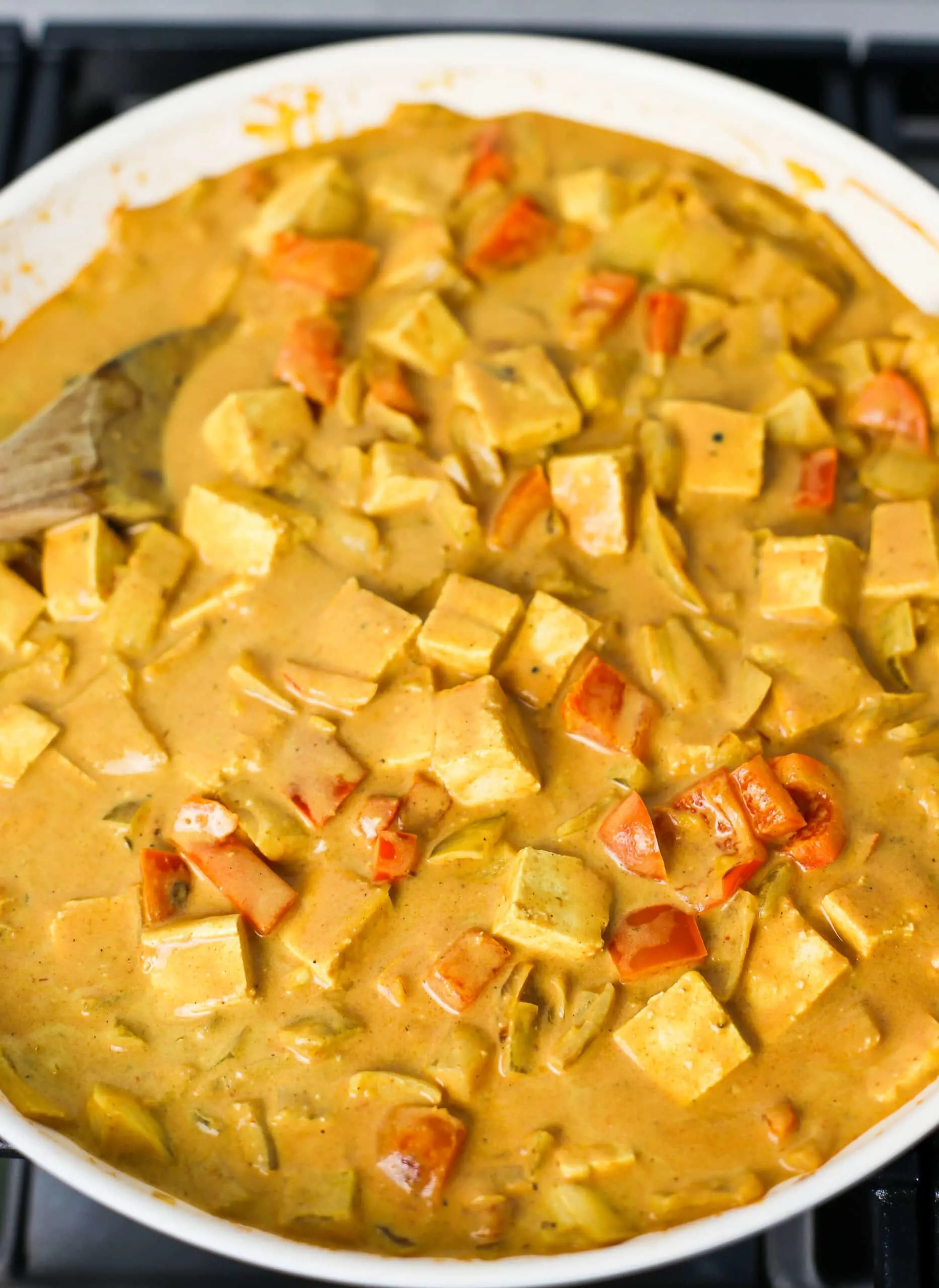 Creamy coconut curry sauce mixed with cubed tofu, and vegetables in a large fry pan.