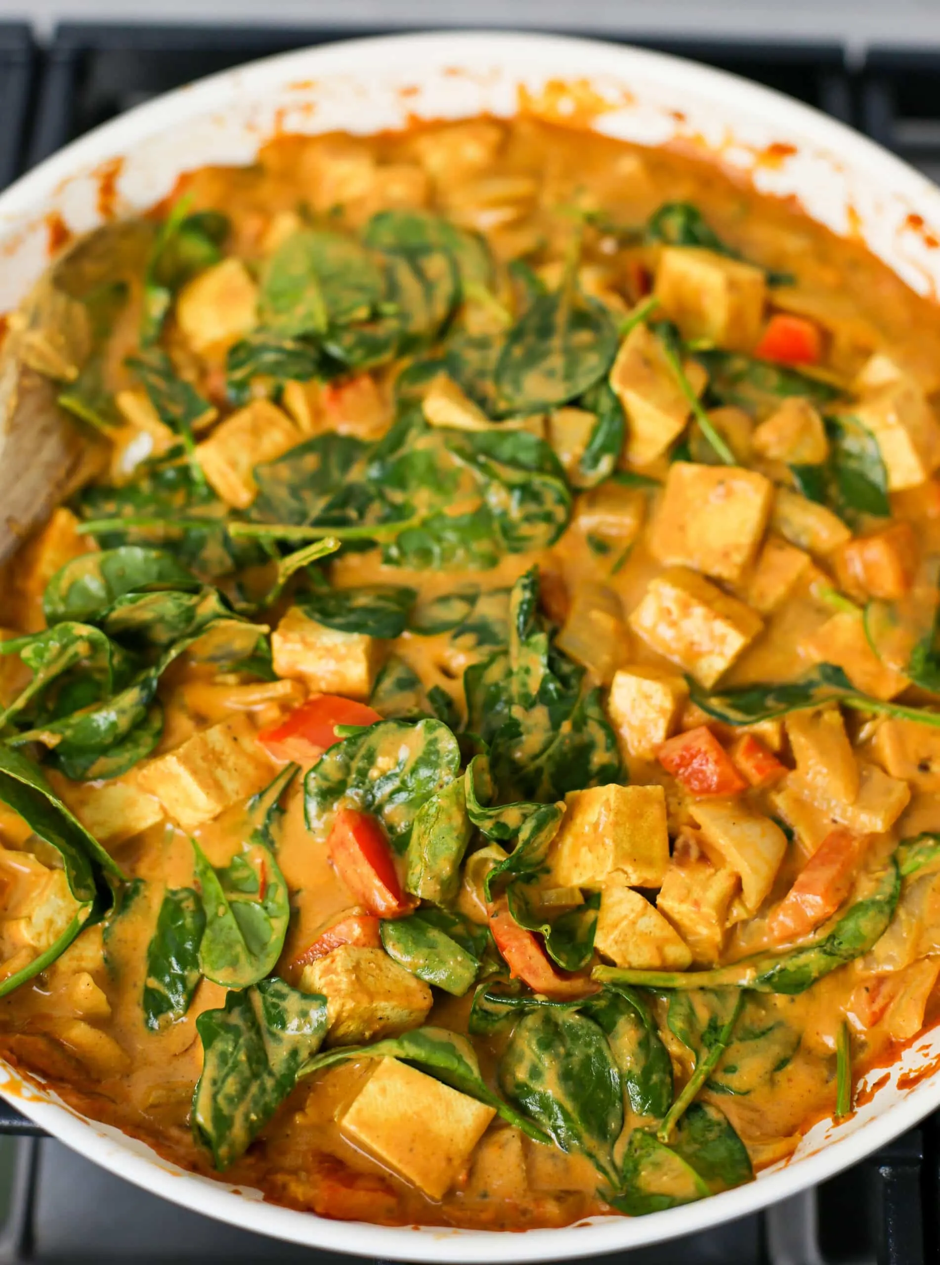 Creamy tofu coconut curry with wilted spinach in a large skillet.