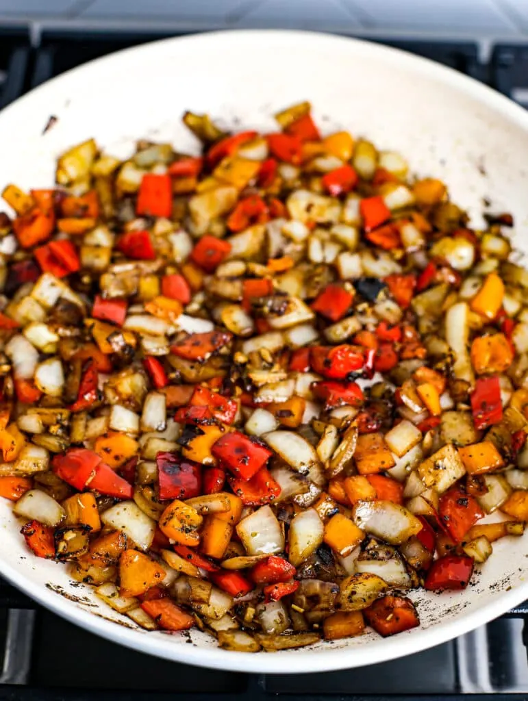 Sautéed chopped white onions, bell peppers, minced garlic, seasonings, and balsamic vinegar in a white frying pan.