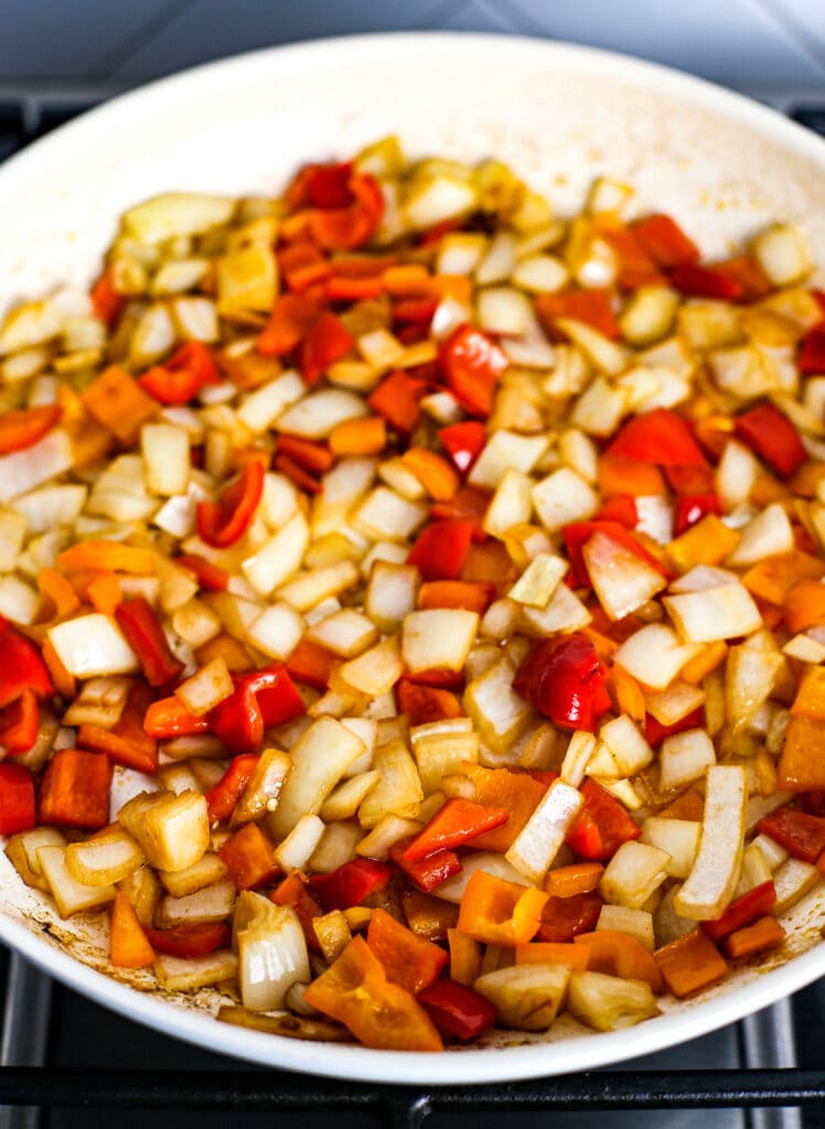Sautéed chopped white onions and bell peppers in a white frying pan.