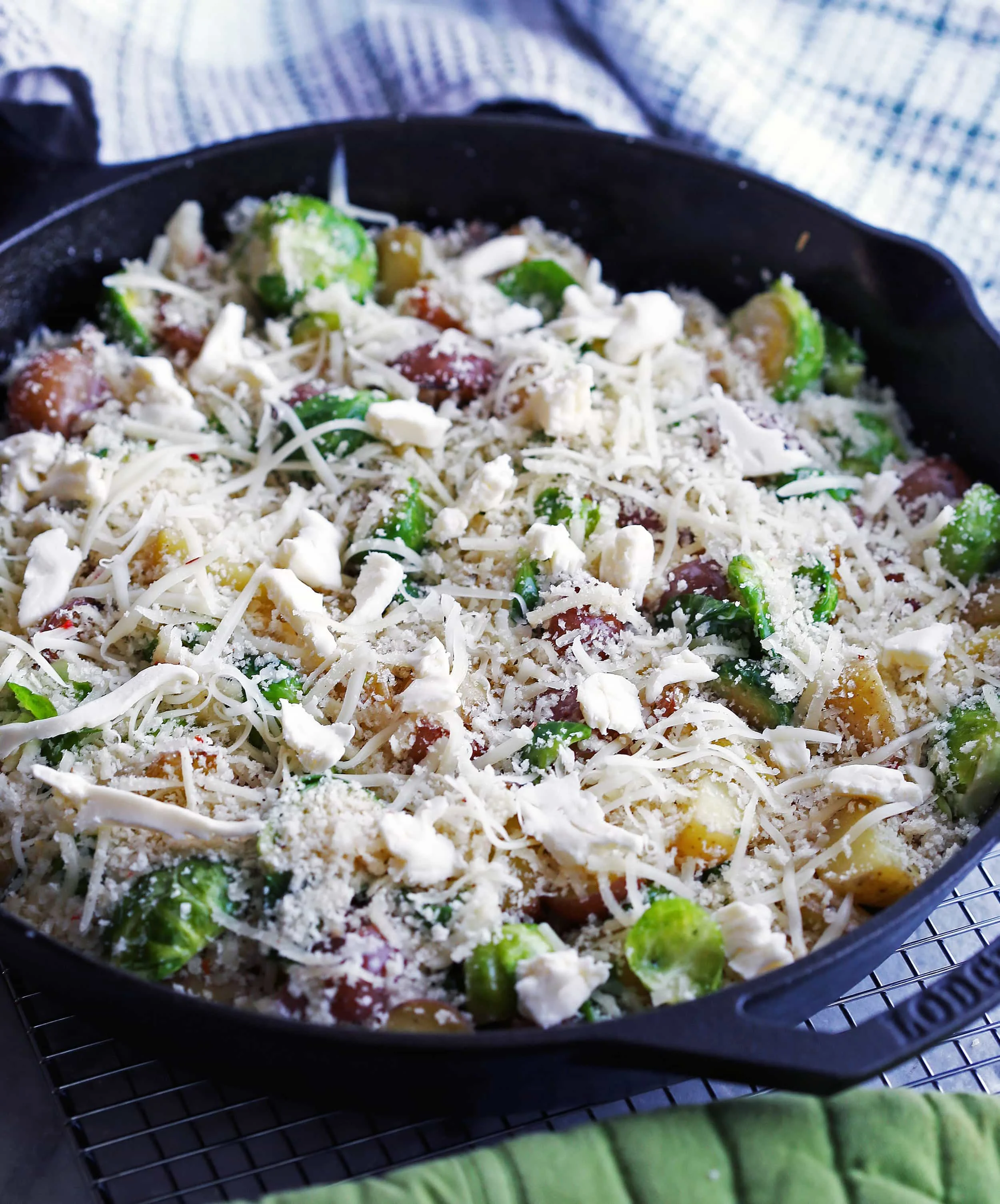 Sautéed onions, baby potatoes, and Brussels sprouts topped with cheese and breadcrumbs in a cast iron skillet.