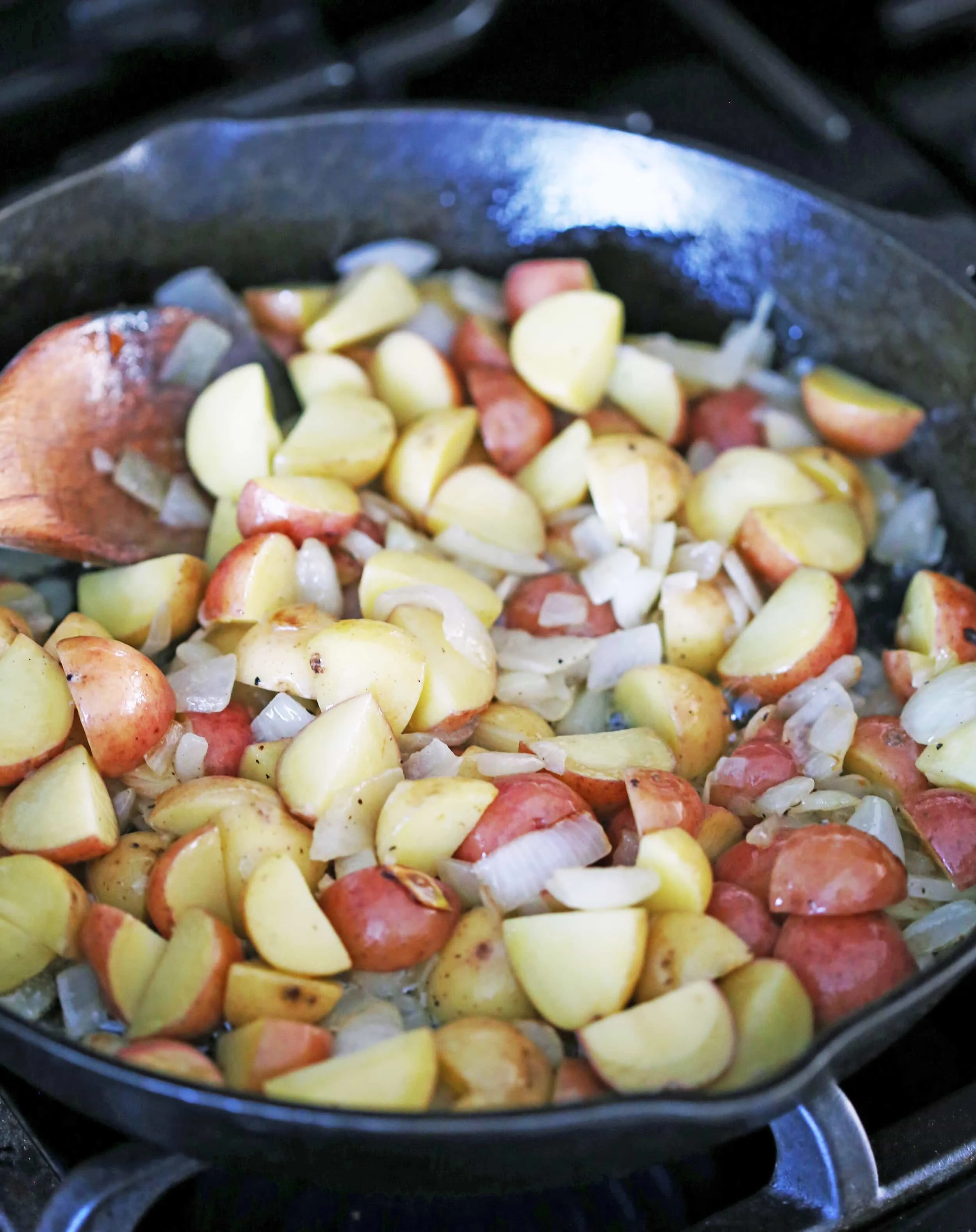 Sautéed onions and chopped baby potatoes in a cast iron skillet.