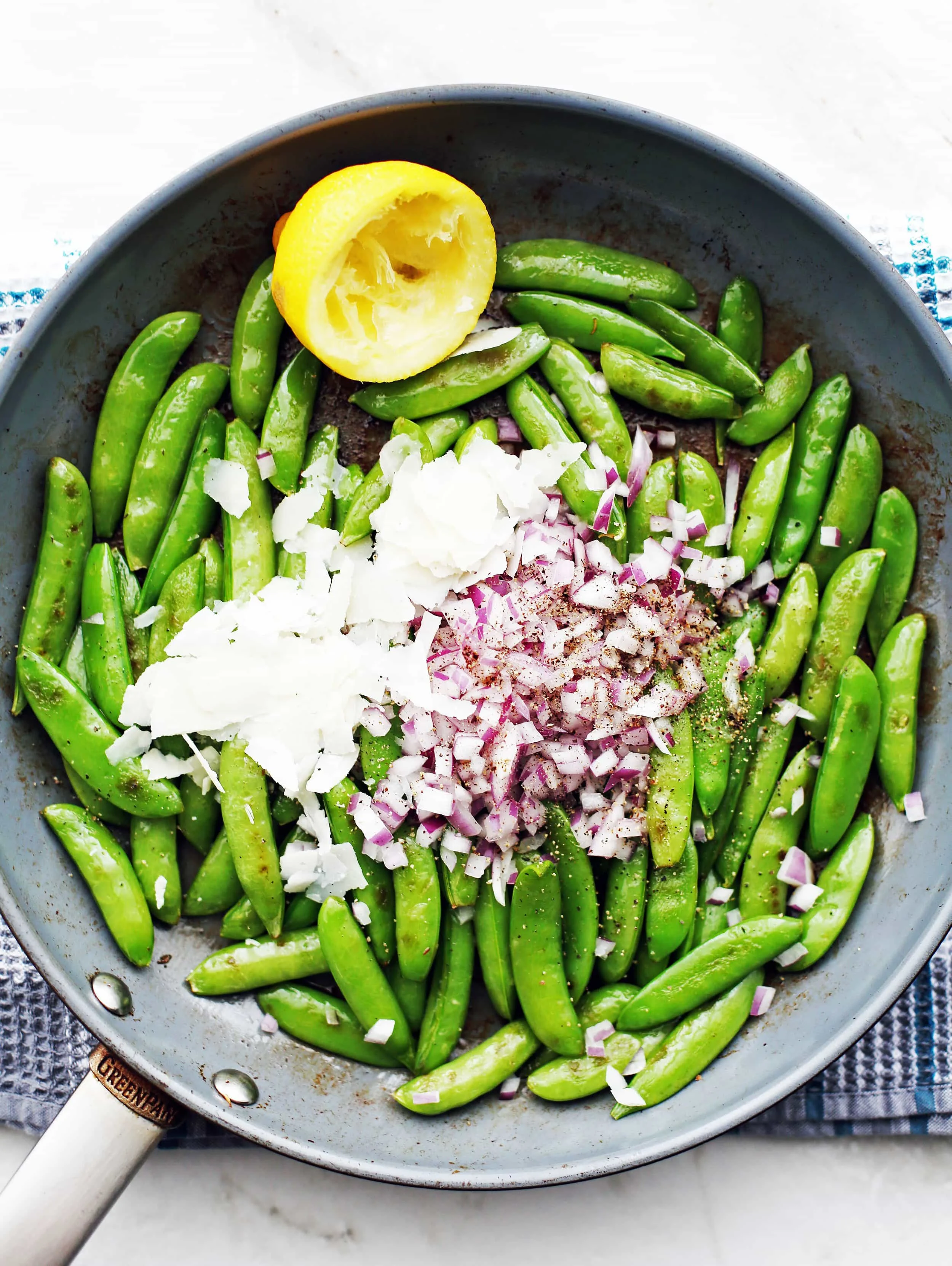 Sauteed sugar snap peas topped with parmesan, red onions, and black pepper in a large frying pan.