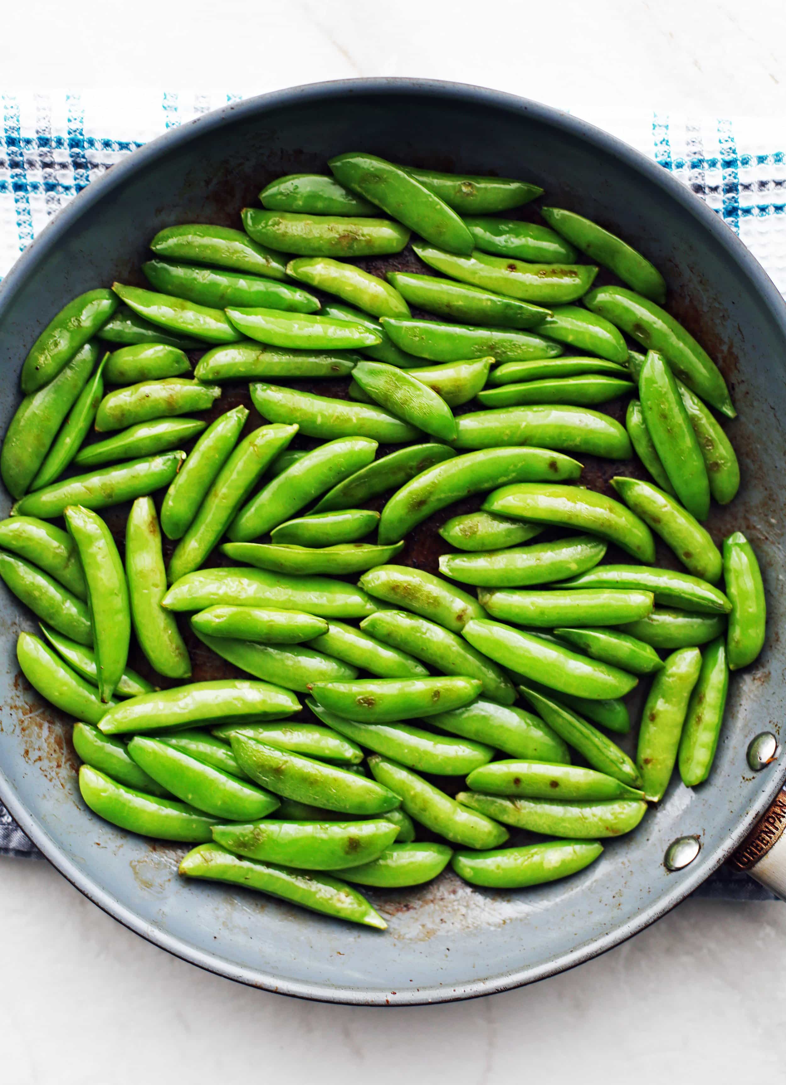 Sauteed sugar snap peas in a blue frying pan.
