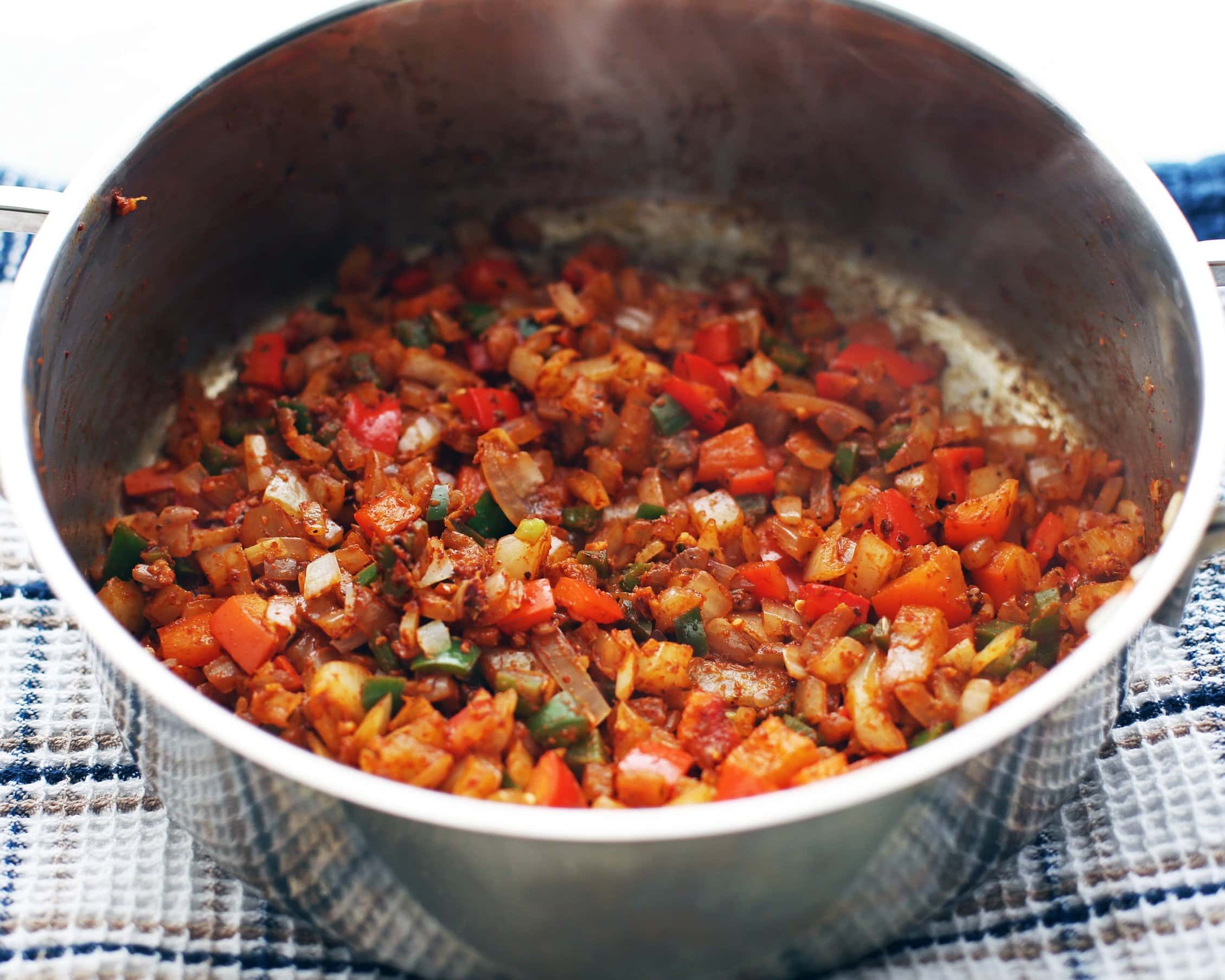 Sautéed peppers, onions, and garlic with spices in a metal pot.