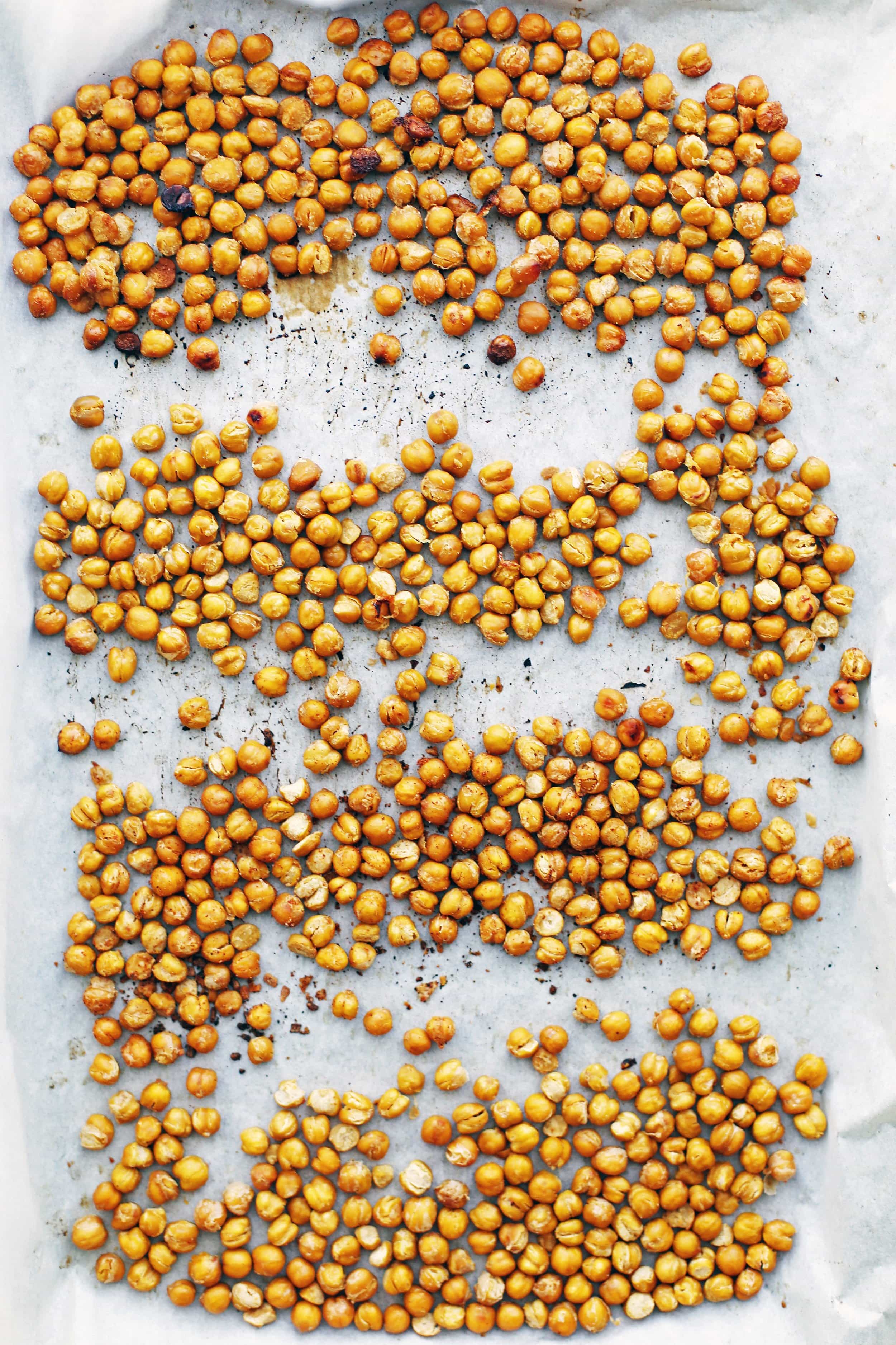 Seasoned roasted chickpeas in a single layer on a parchment paper lined baking sheet.
