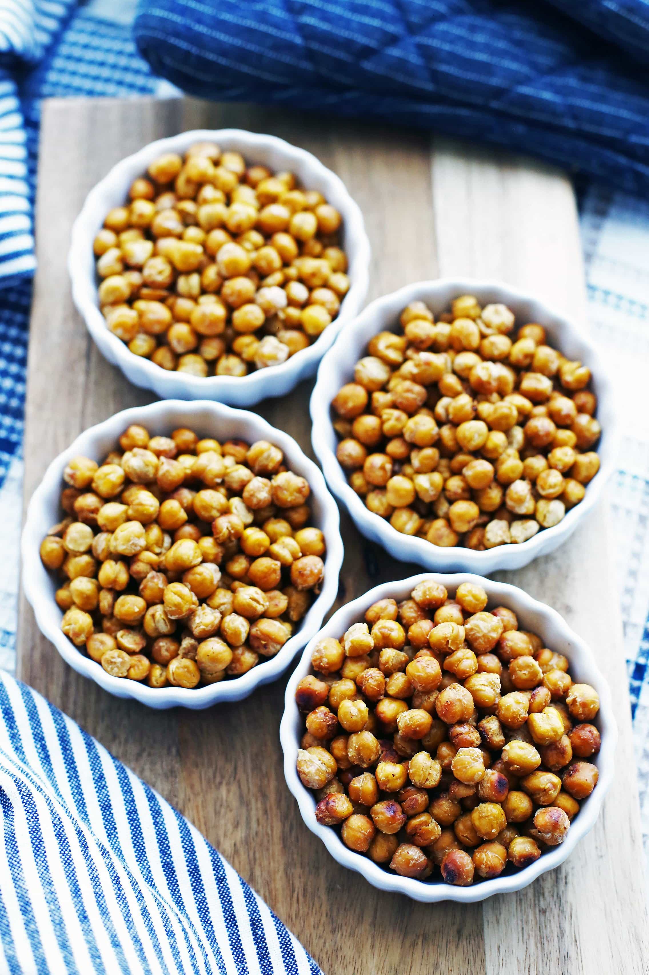 Crispy seasoned roasted chickpeas in four mini porcelain tart pans on a long wooden board.