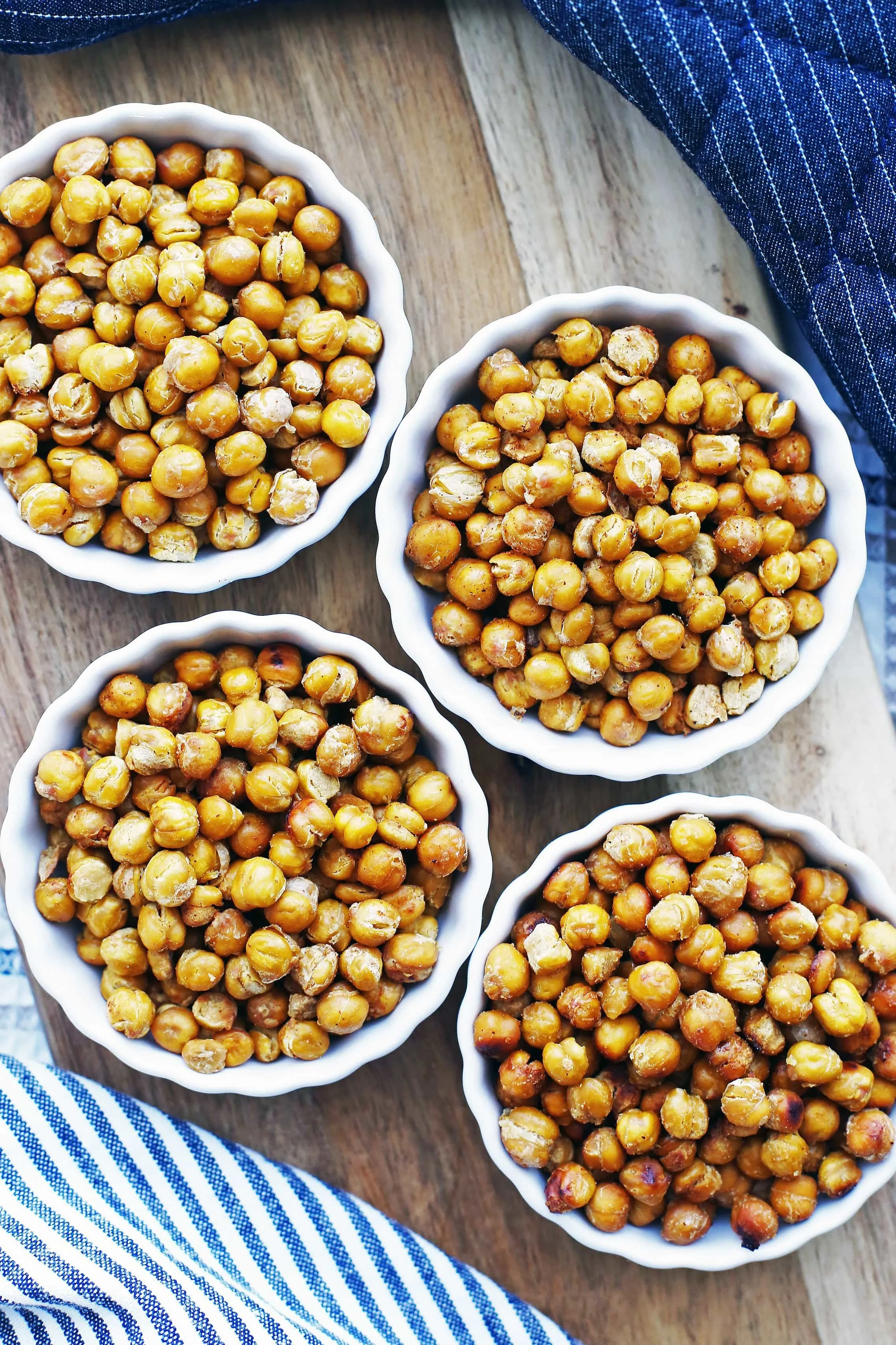 Overhead view of salt and vinegar, taco, honey garlic, and brown sugar lemon roasted chickpeas separated into four porcelain tart pans.