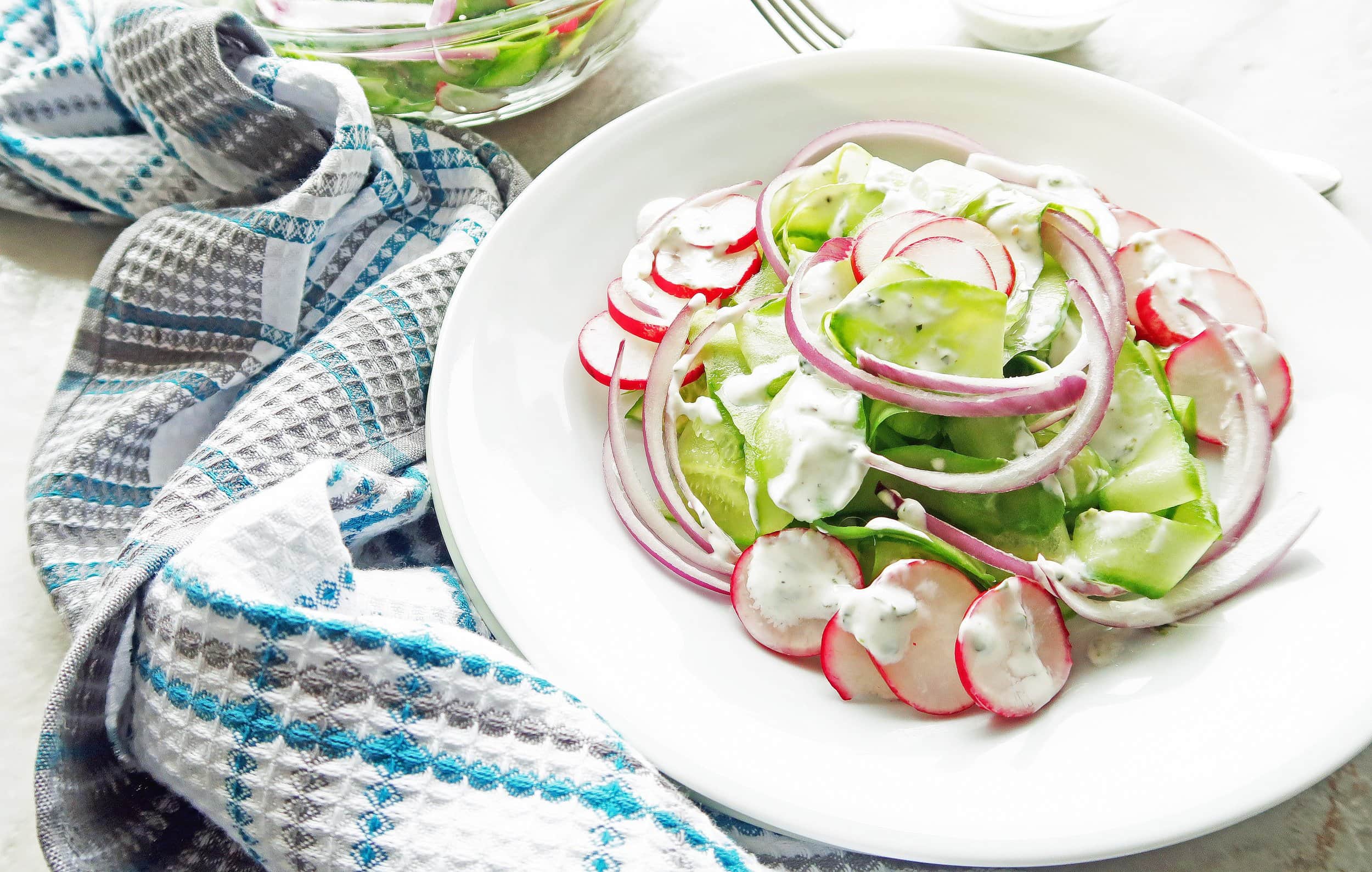 Shaved Cucumber Salad with Lime-Mint Yogurt Dressing on a white plate; a kitchen towel draped on the side of the plate.