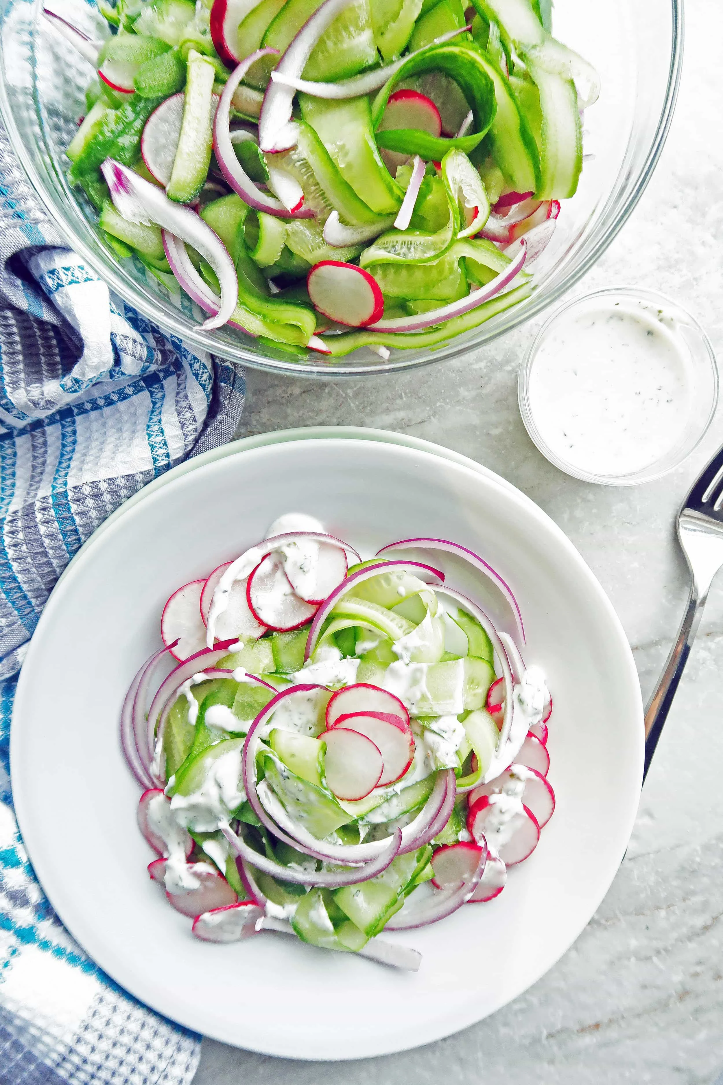 Shaved Cucumber Salad with Lime-Mint Yogurt Dressing on a white plate with more undressed salad, dressing, and fork to its side.