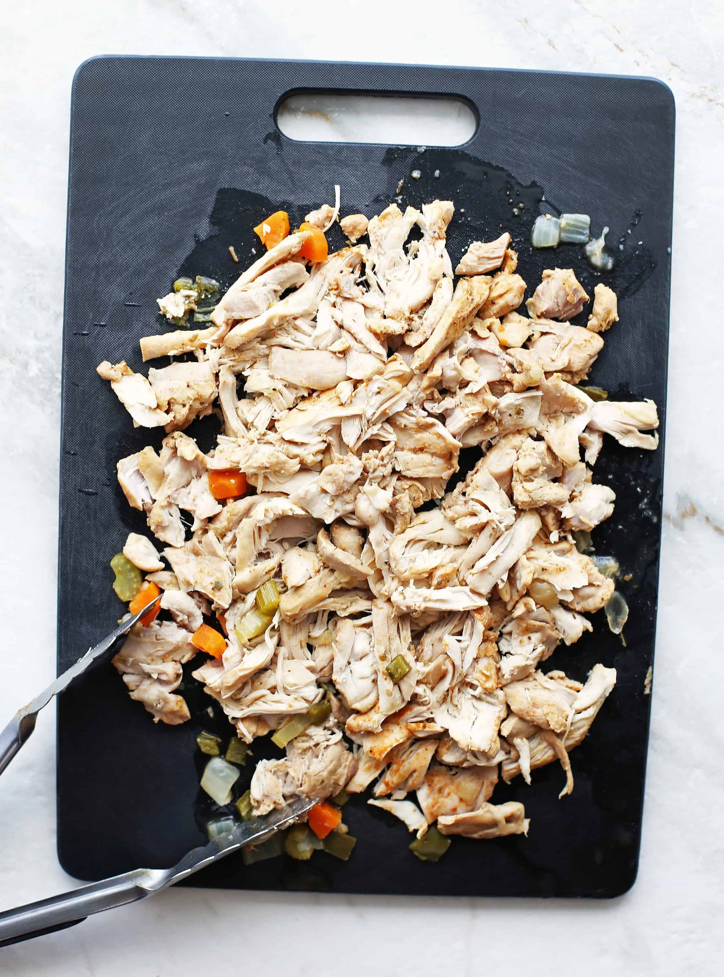 Cooked shredded chicken thighs on a black cutting board.