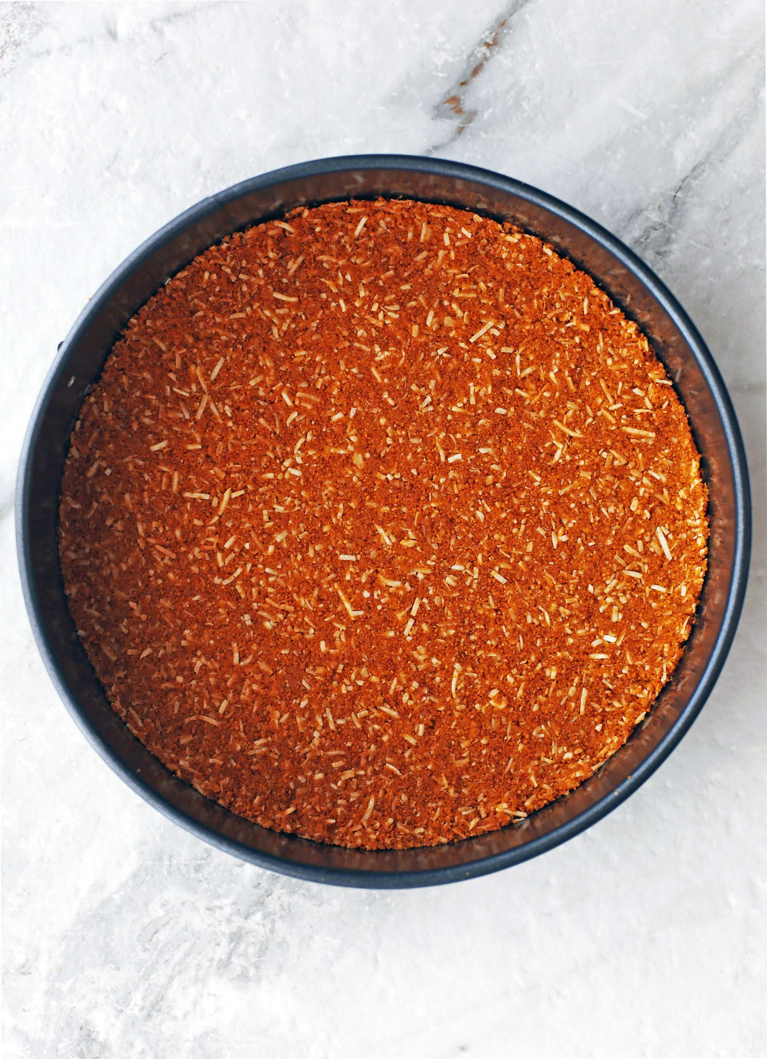 A toasted coconut and graham cracker crust pressed onto the base of a round springform pan.