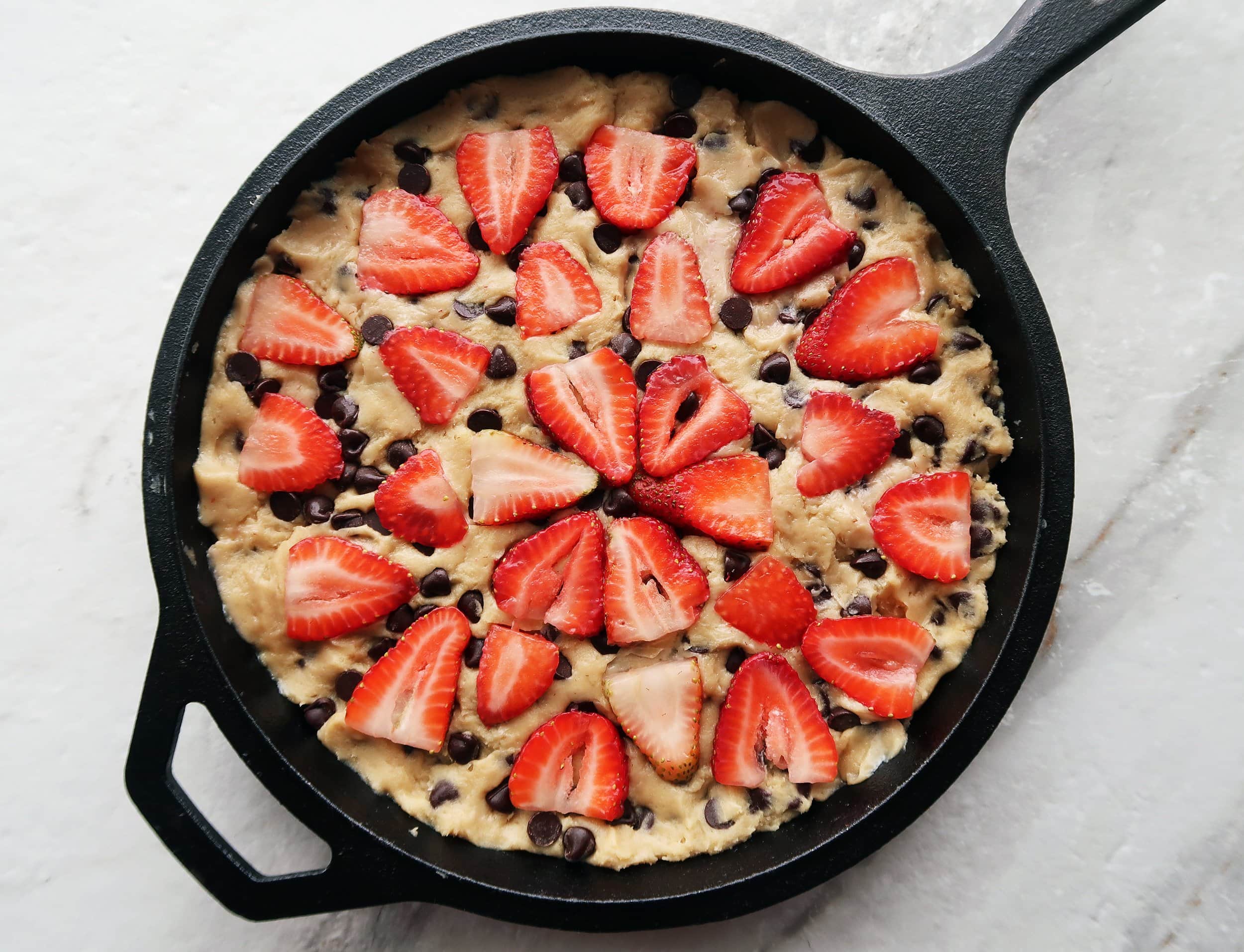 Cookie dough in a skillet topped with strawberries.