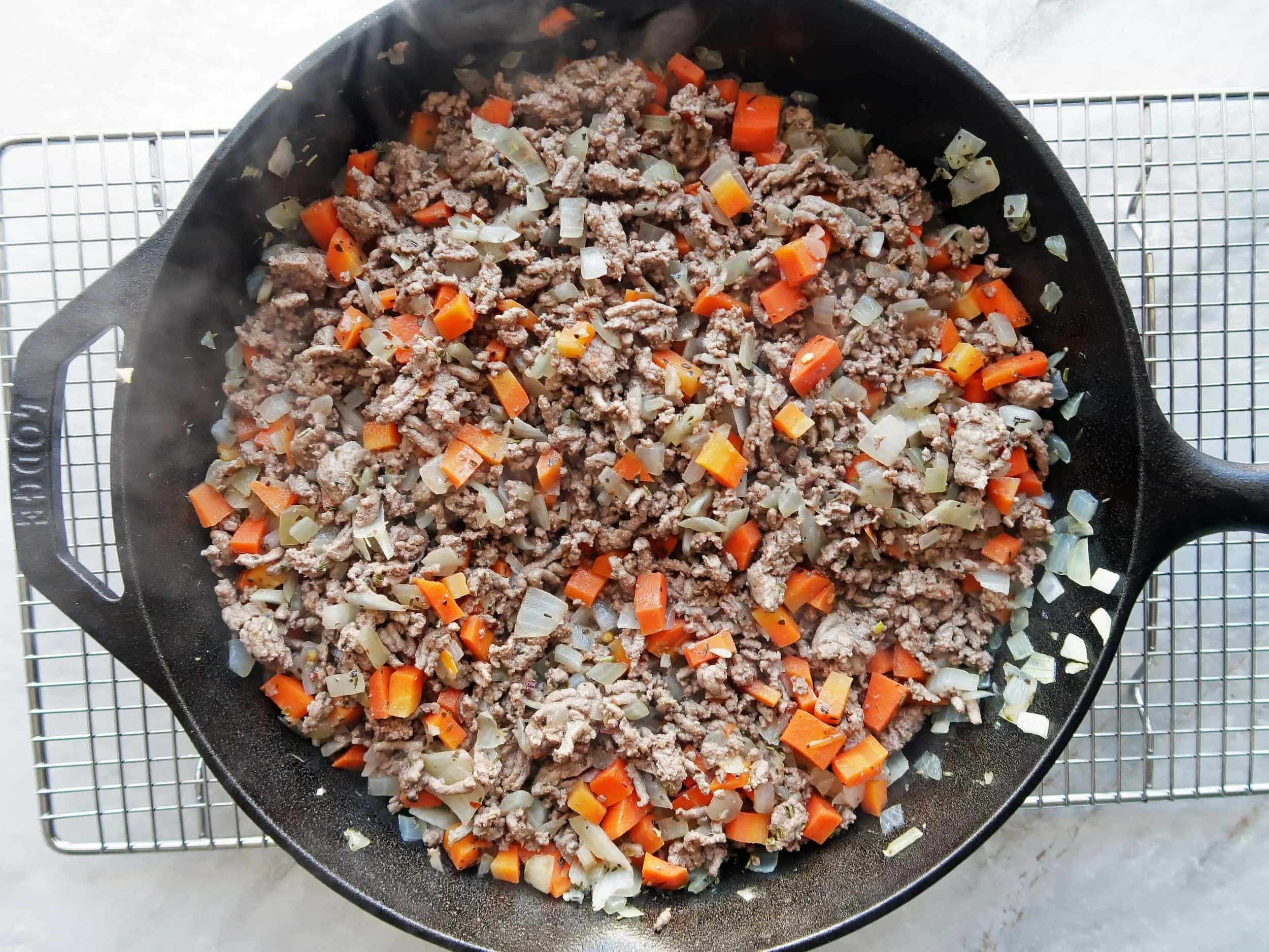 A cast iron skillet full of sauteed ground beef, chopped onions, and bell peppers.