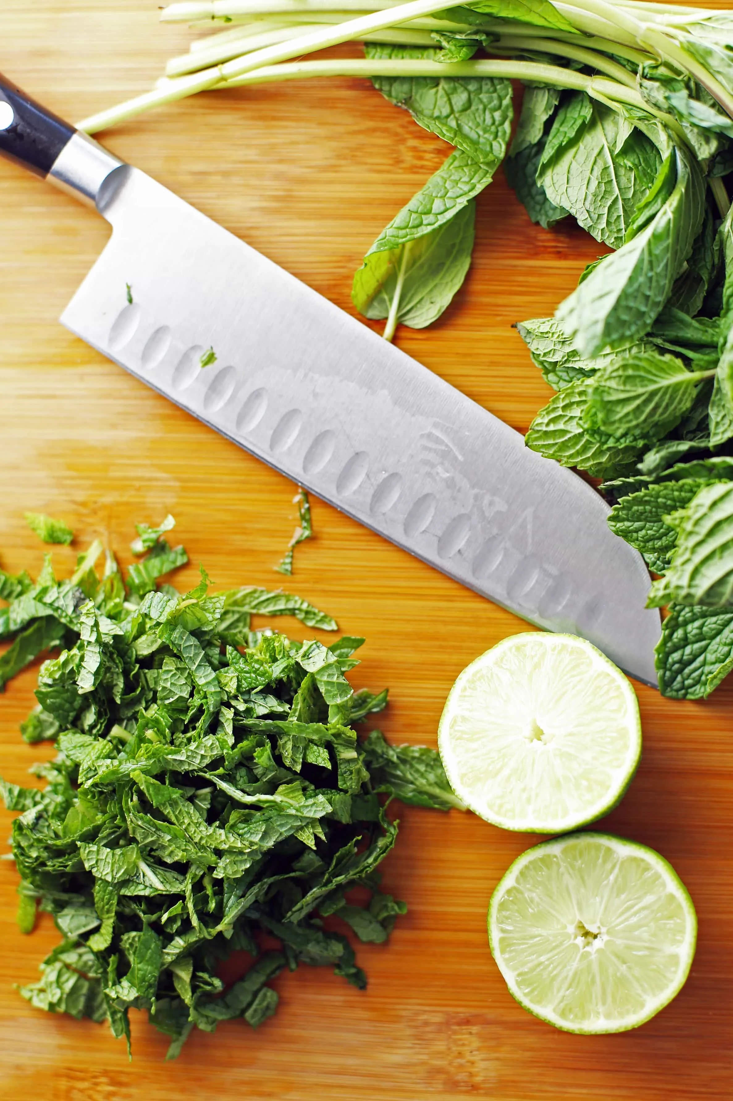 Thinly sliced fresh mint, a lime cut in half, and a large knife on a wooden cutting board.