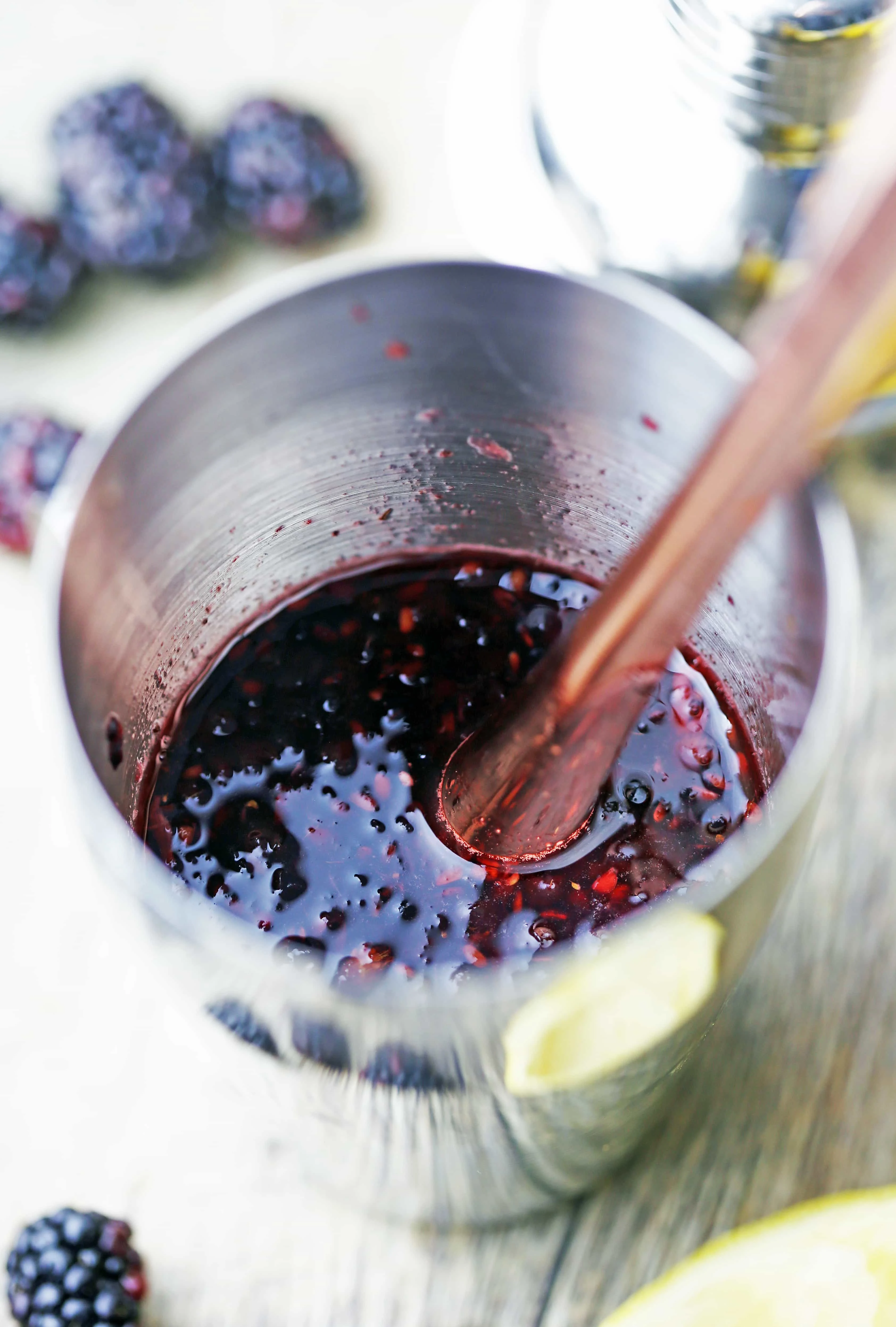 Smashed blackberries, lemon juice, and simple syrup in a stainless steel cocktail shaker.