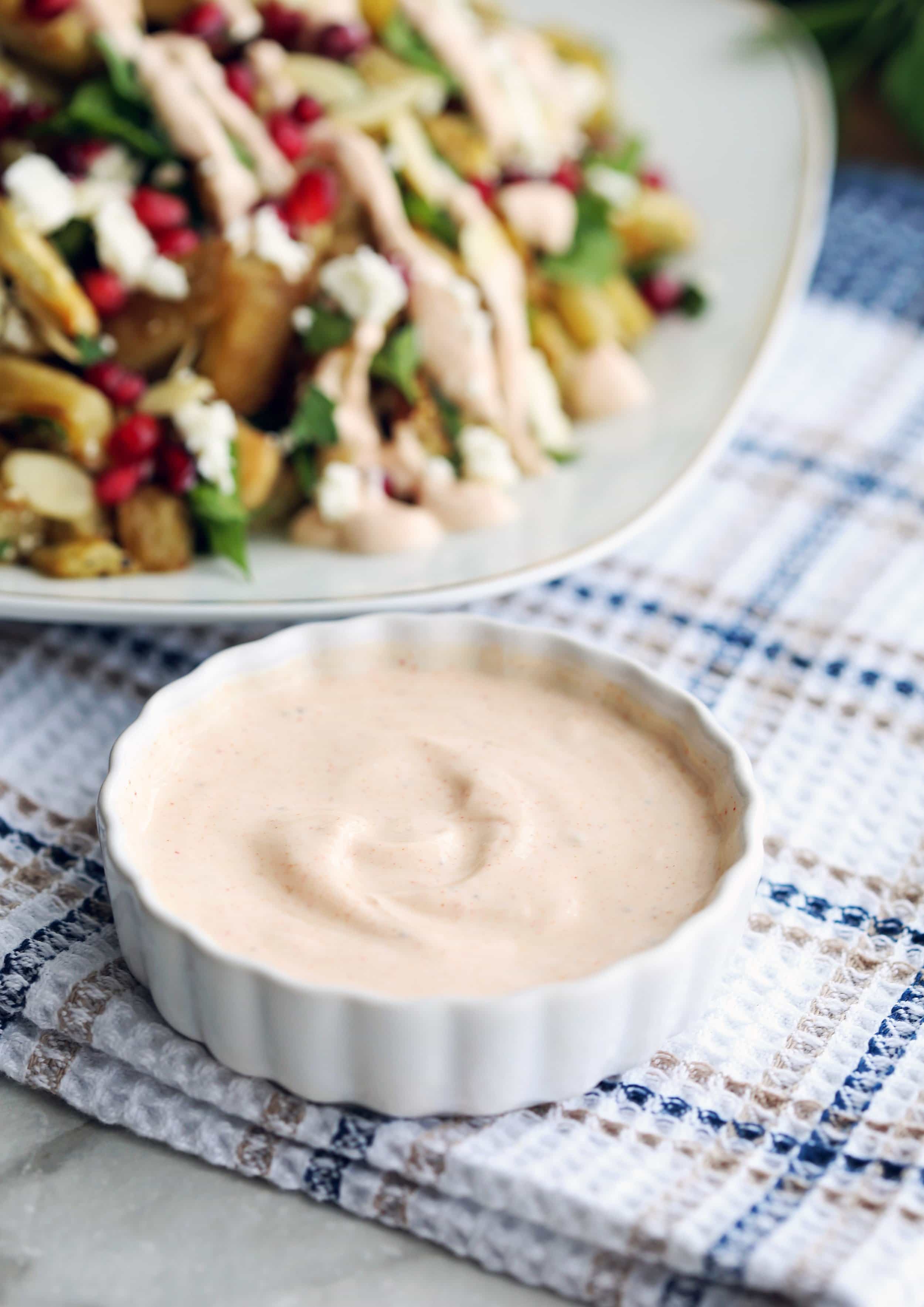 A closeup of a small bowl containing smoked paprika yogurt dressing with eggplant salad in the background.