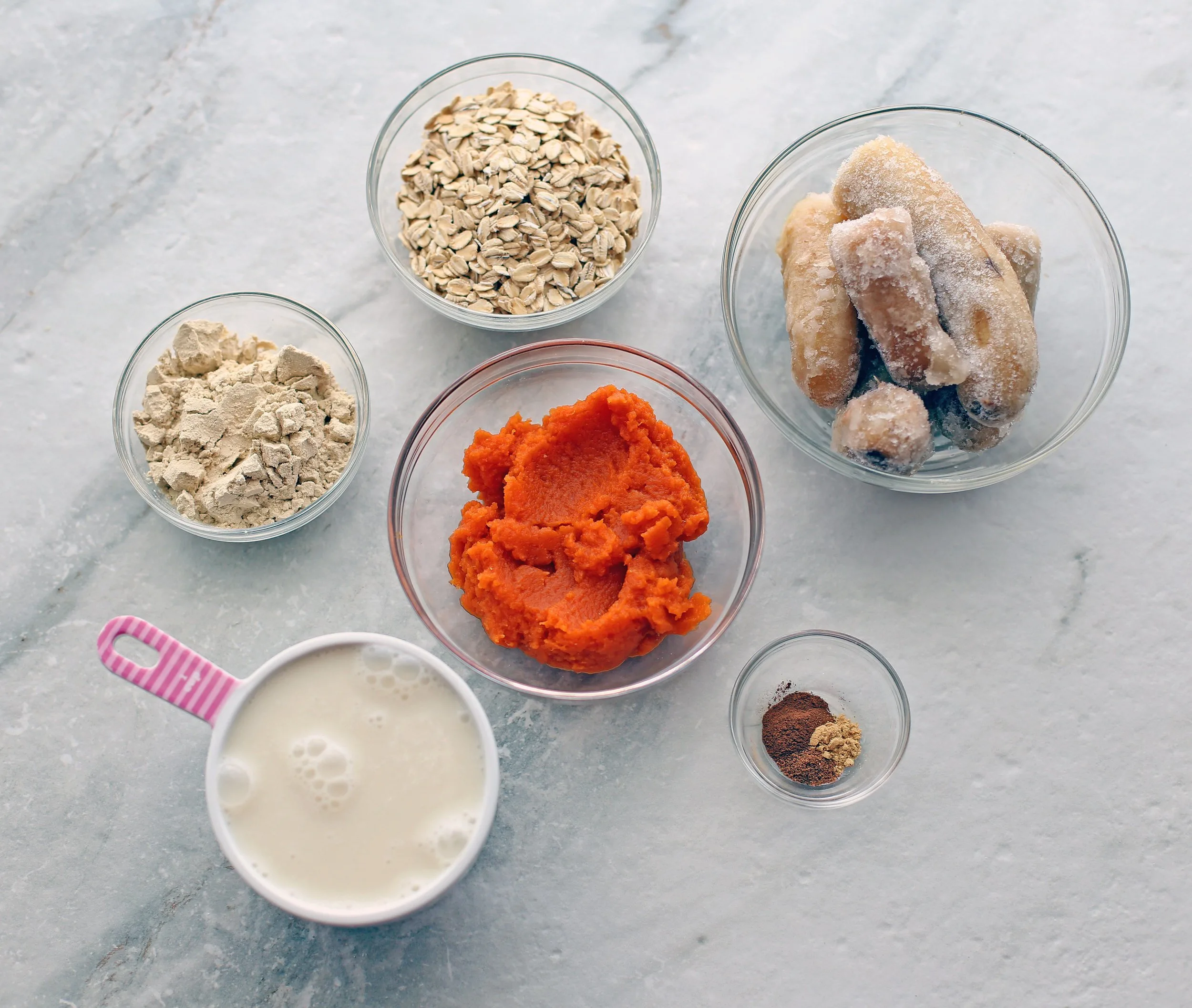 Overhead view of almond milk, pumpkin puree, frozen banana, spices, protein powder, and oatmeal.