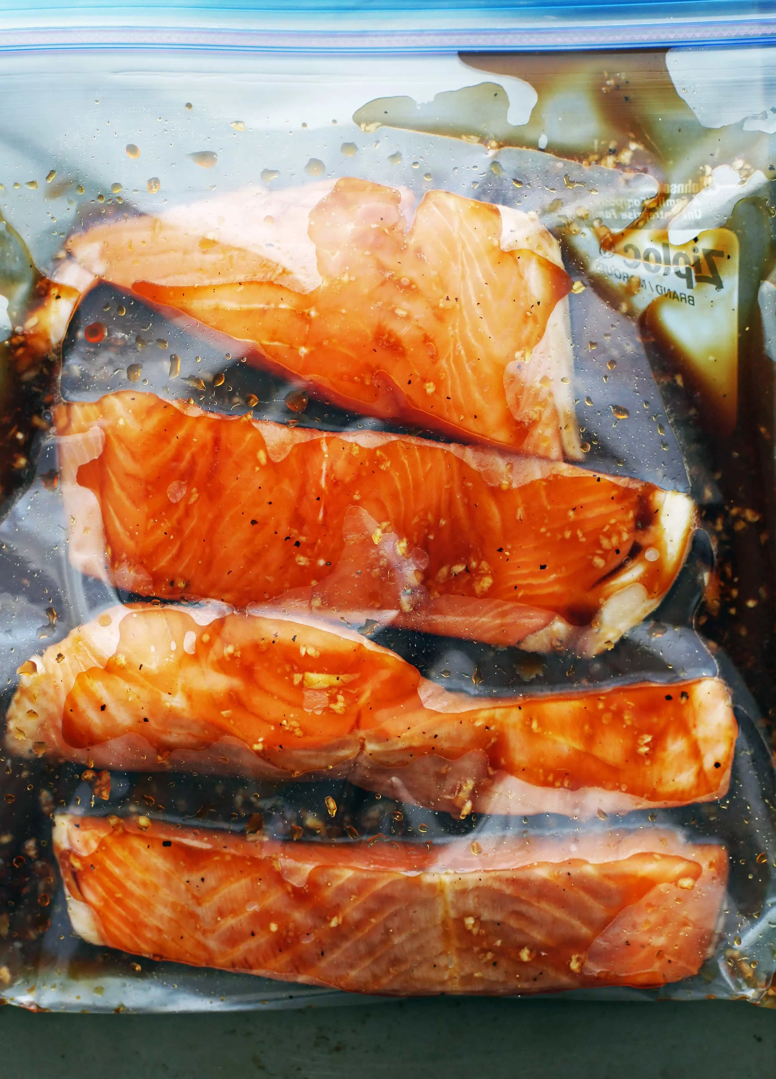 A large resealable plastic bag containing four salmon fillets and soy-maple marinade.