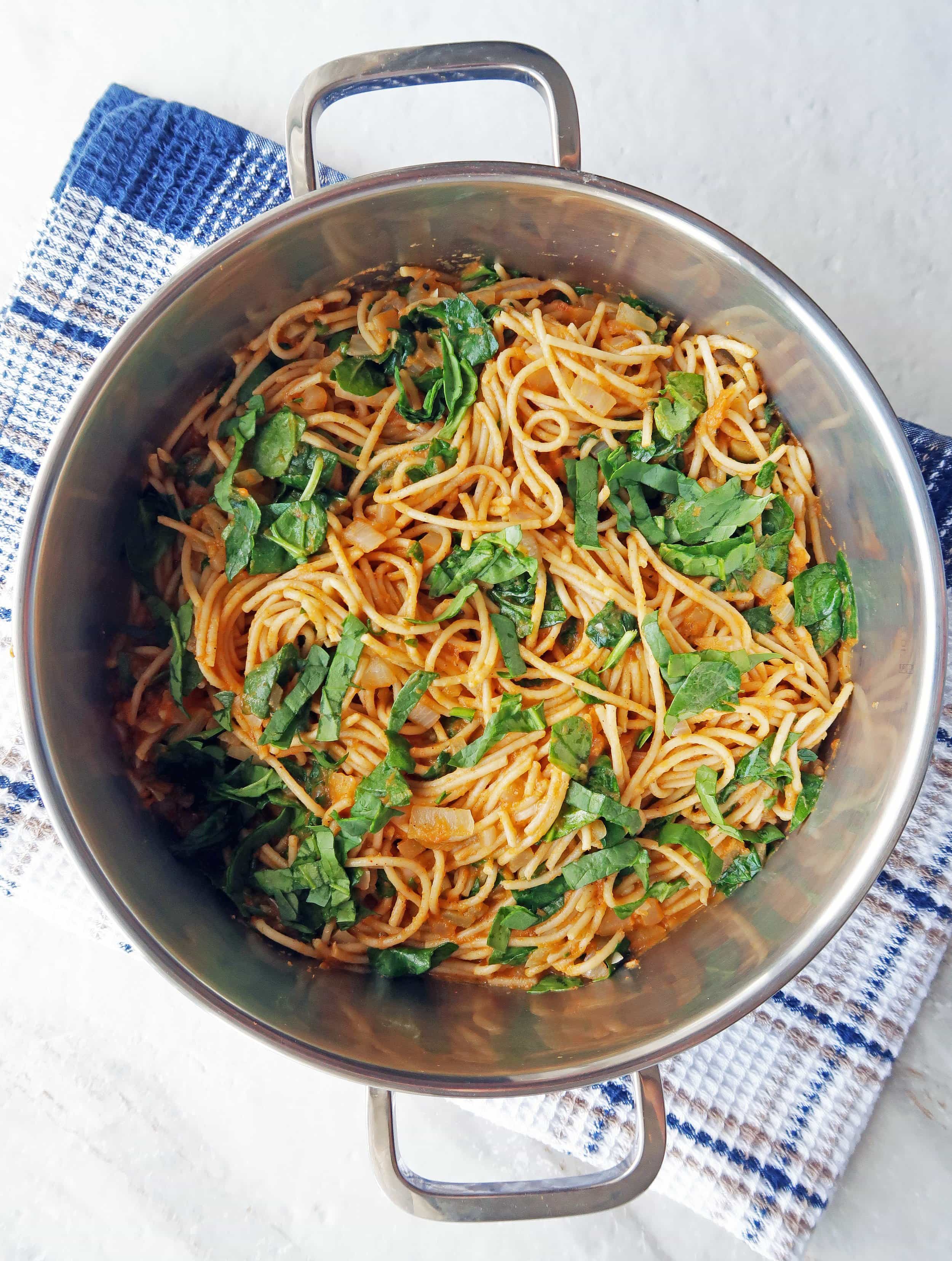 Spaghetti with creamy pumpkin sauce and fresh spinach in a large metal pot.