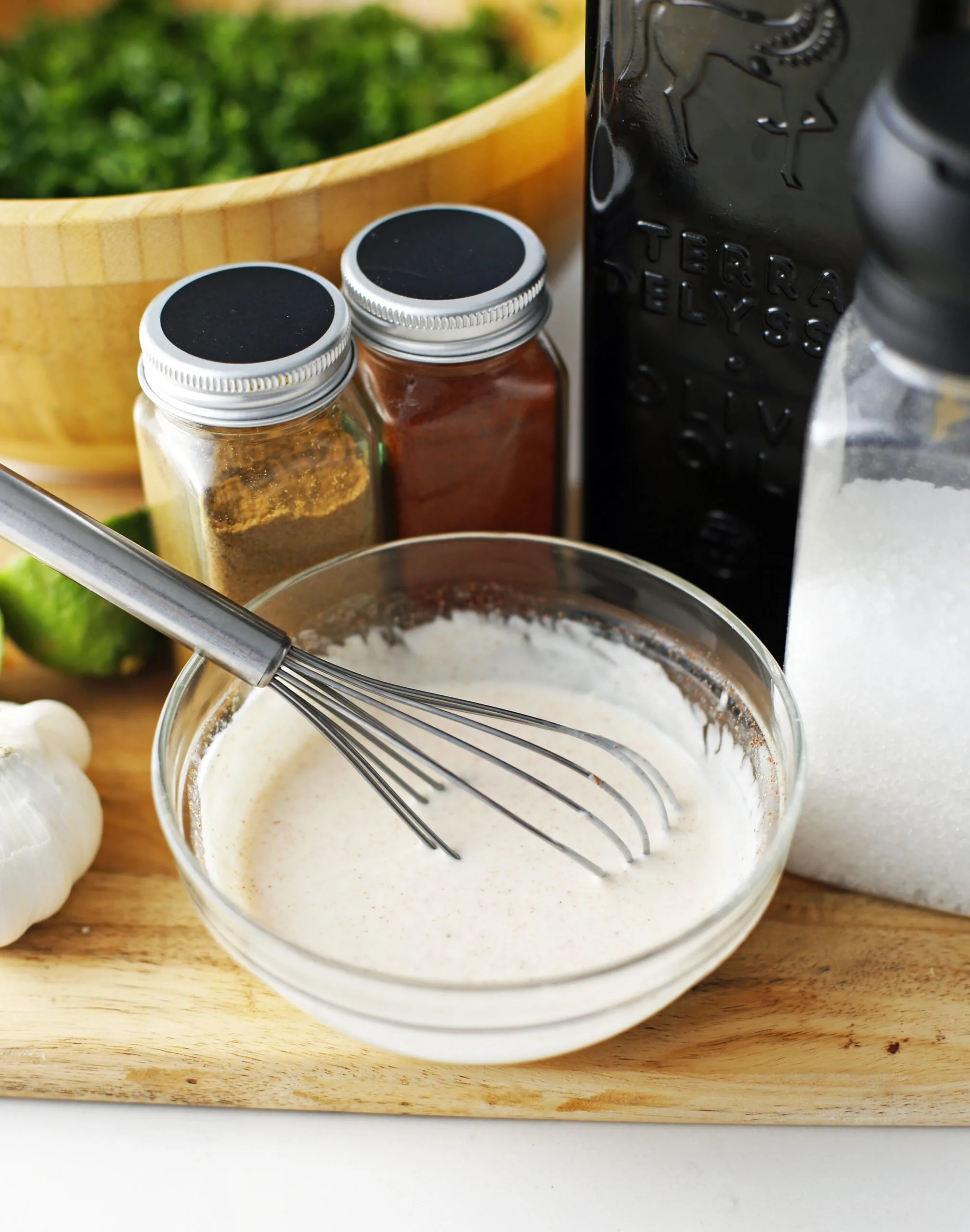 Garlic lime yogurt dressing in a glass bowl with a wired whisk.