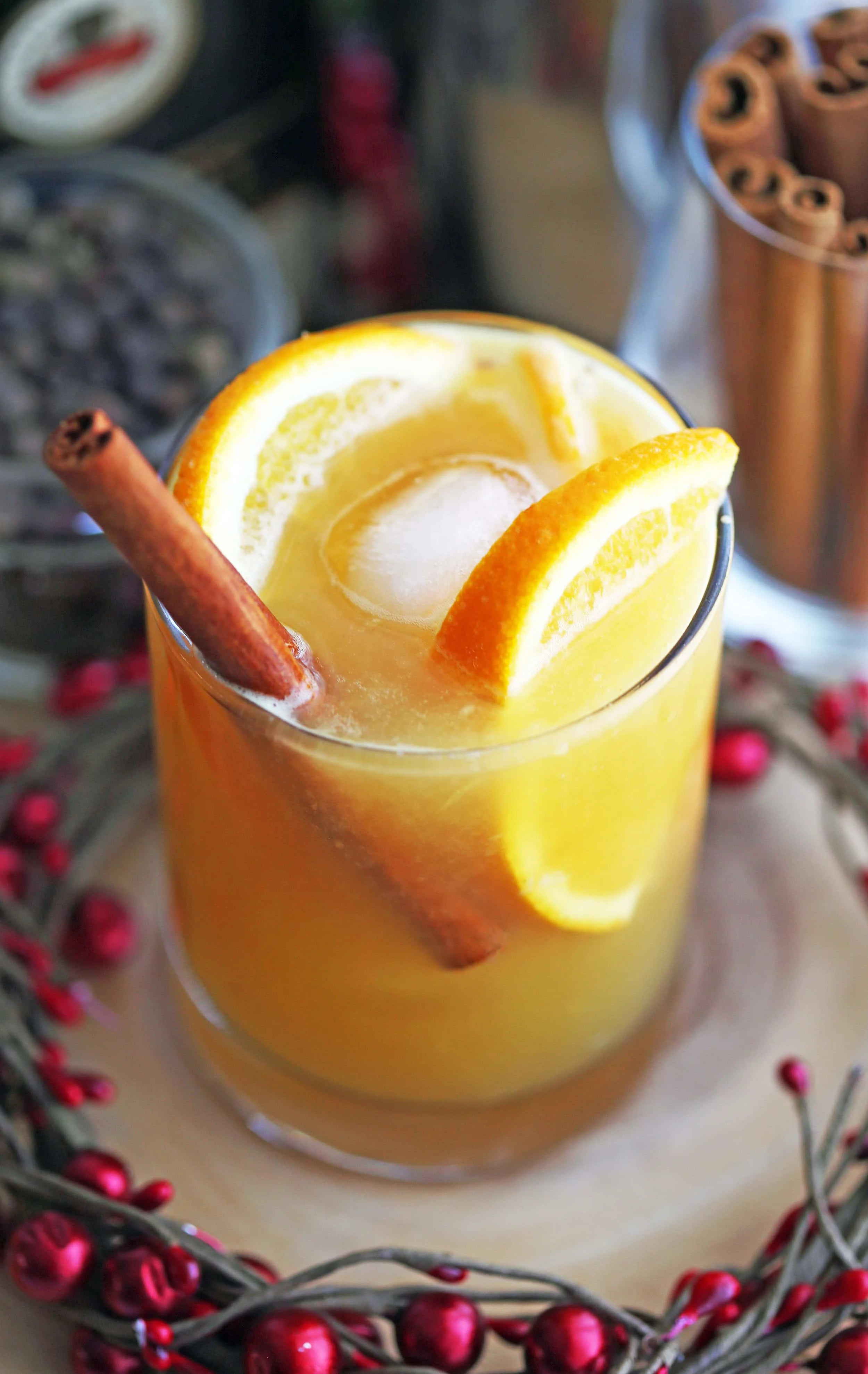 A closeup of a spiced orange brandy spritzer cocktail garnished with orange slices and a cinnamon stick in a glass.