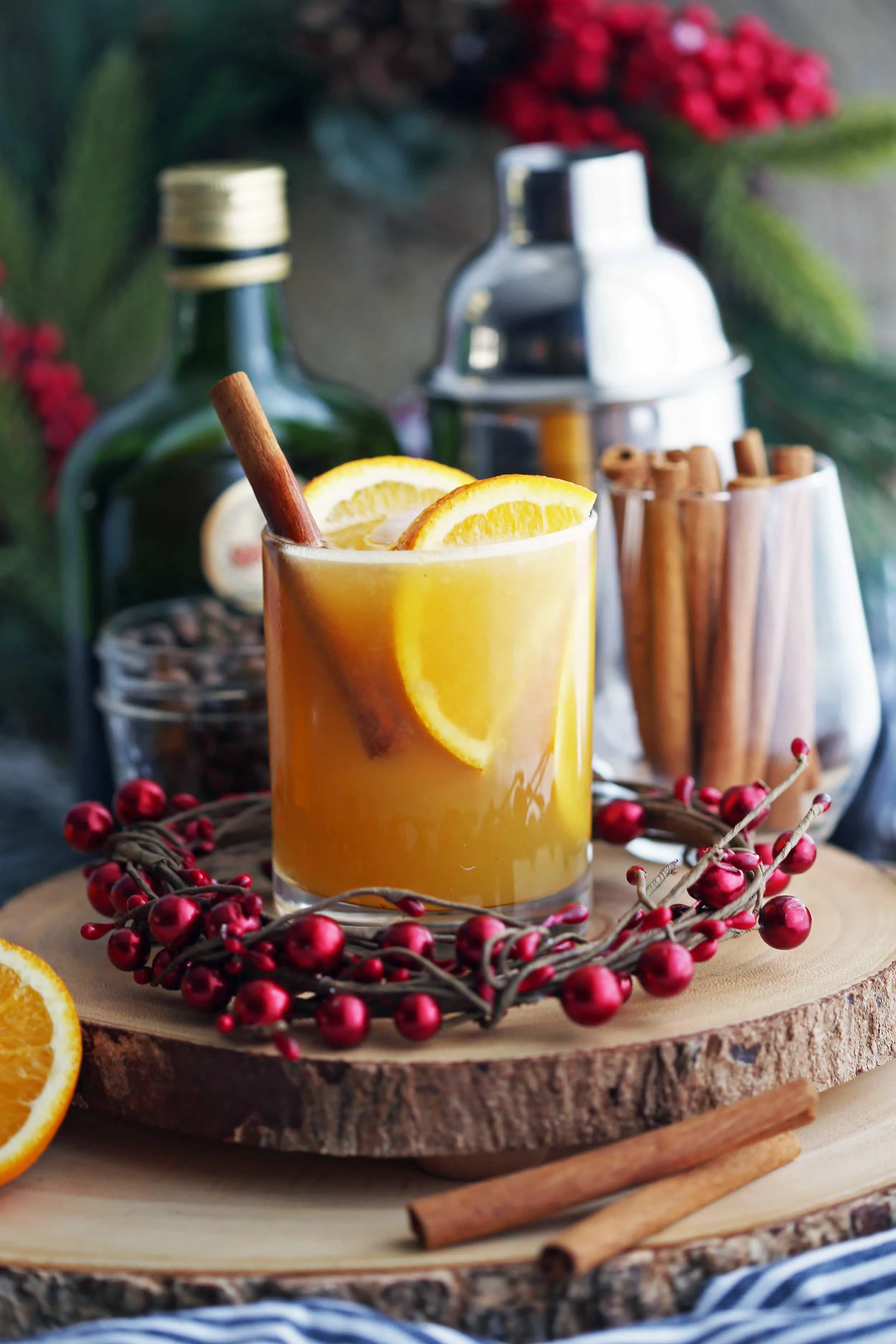 A wooden platter containing a glass of spiced orange brandy spritzer cocktail with orange slices and a cinnamon stick.