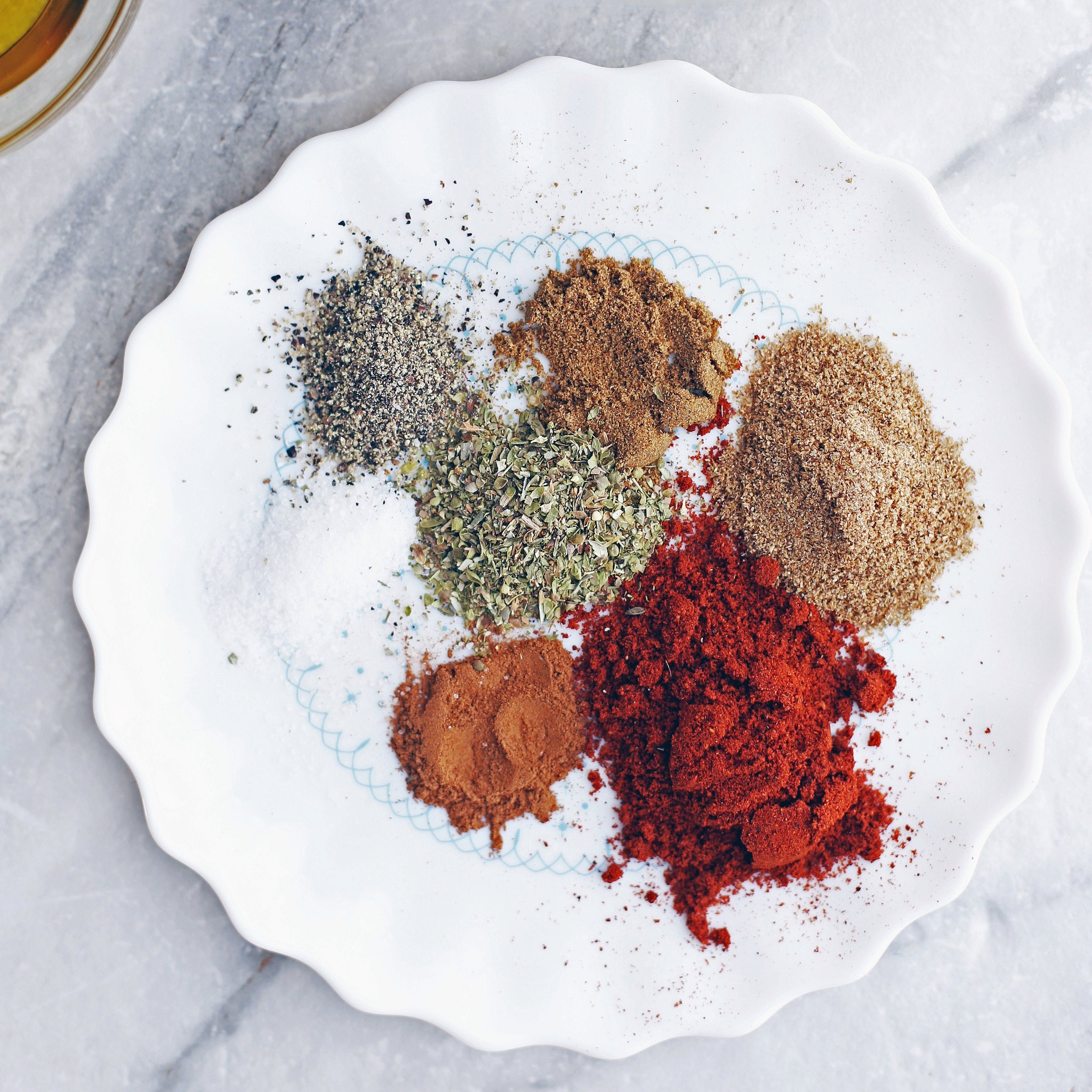 A plate of chili powder, ground coriander, cumin, cinnamon, oregano, black pepper, and salt.