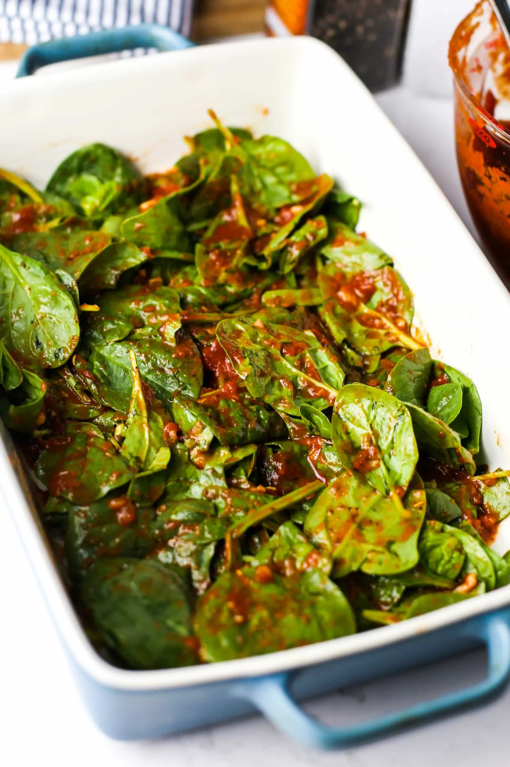 Marinara sauce mixed with fresh baby spinach in blue and white rectangular casserole dish.