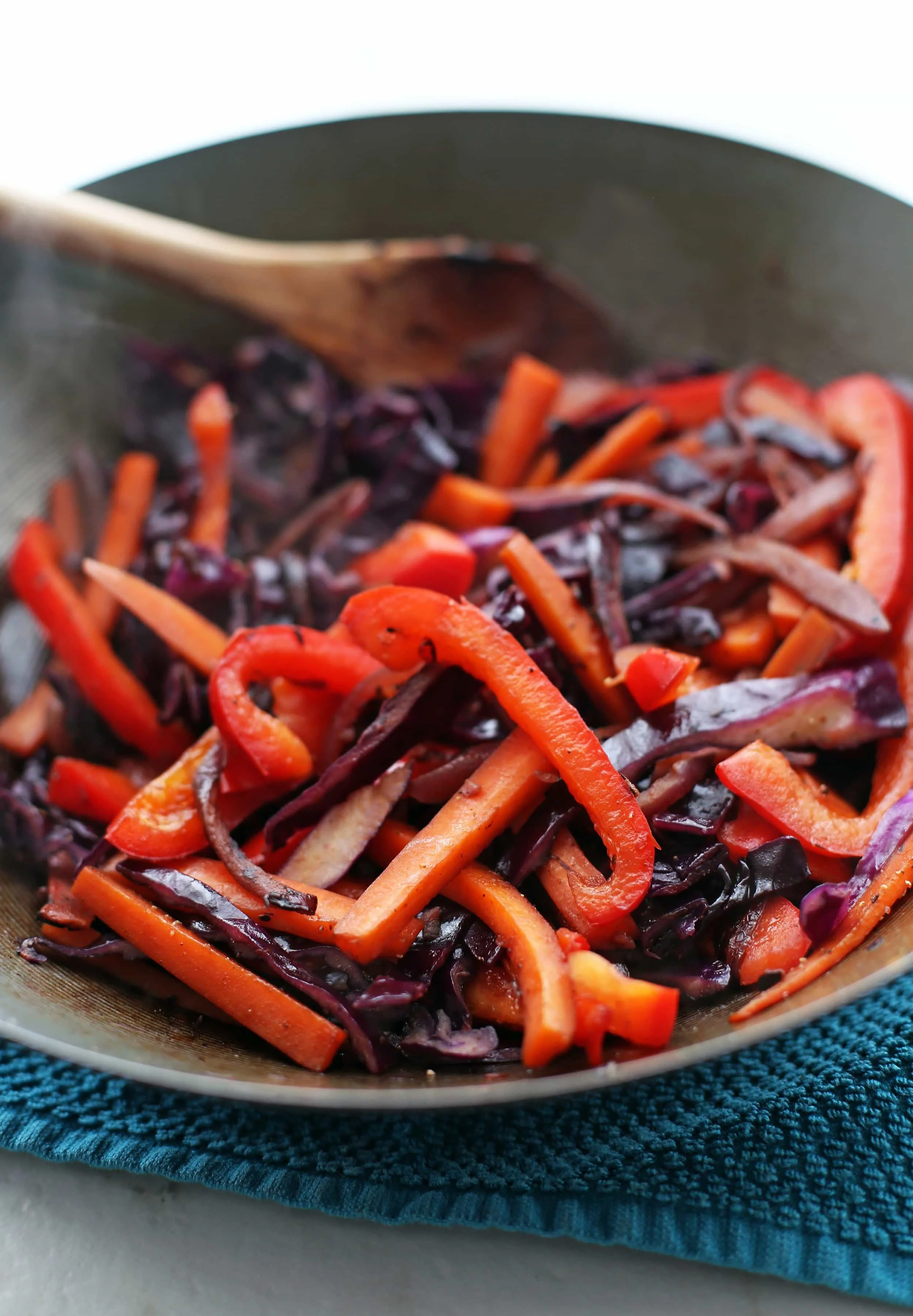 Stir-fried onions, bell pepper, red cabbage, and carrots in a large wok.