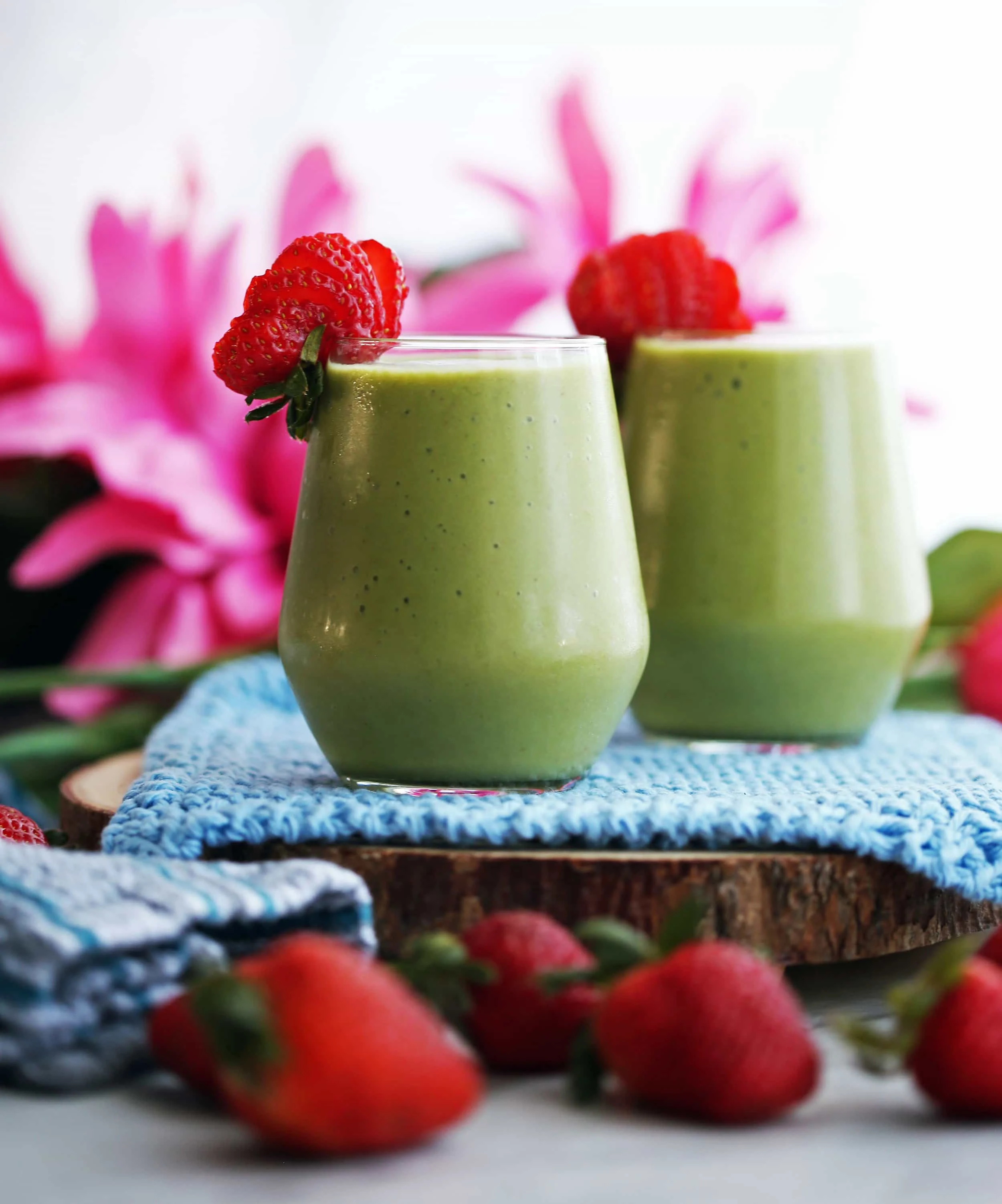 A side view of two glasses of creamy strawberry avocado spinach green smoothies with strawberries garnish on glass rims.