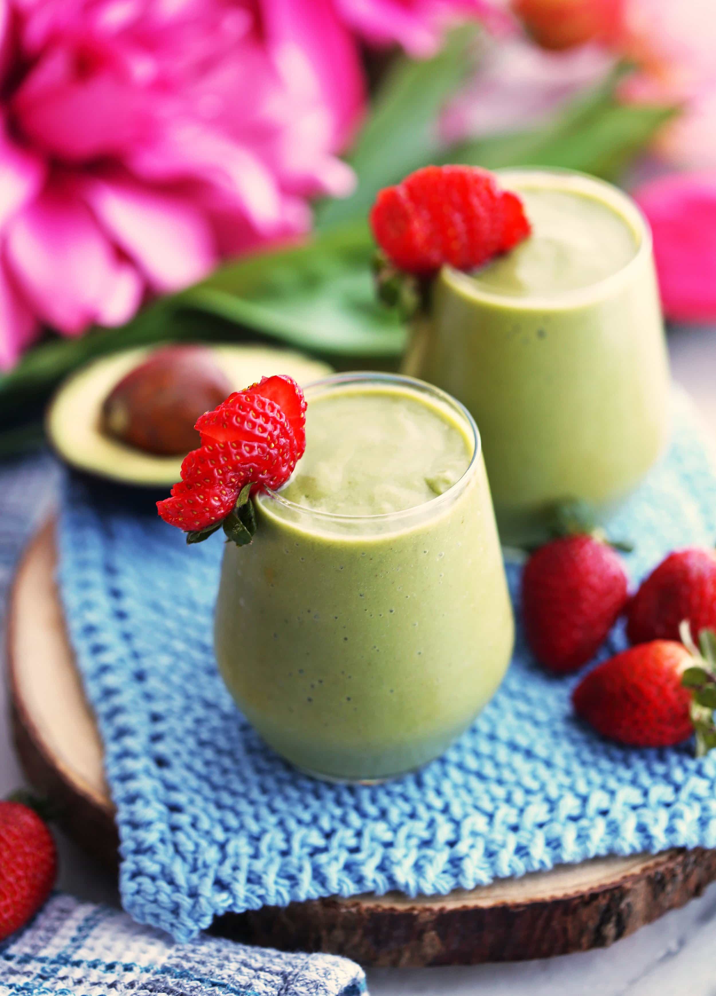 A top angled view of two green smoothies made with avocado, strawberries, spinach, and almond milk.
