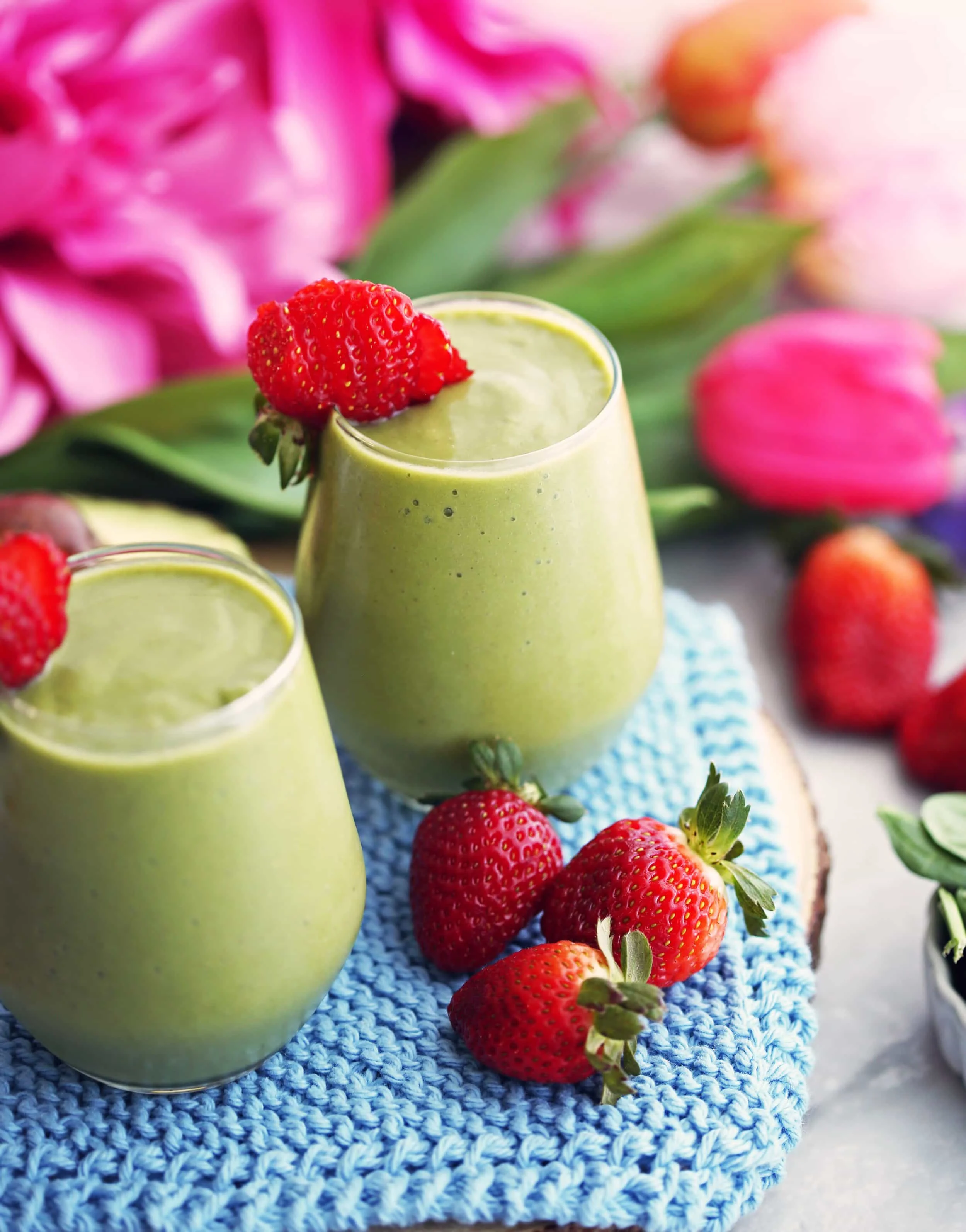 Two glasses of strawberry avocado spinach green smoothies with fresh strawberries on the side.