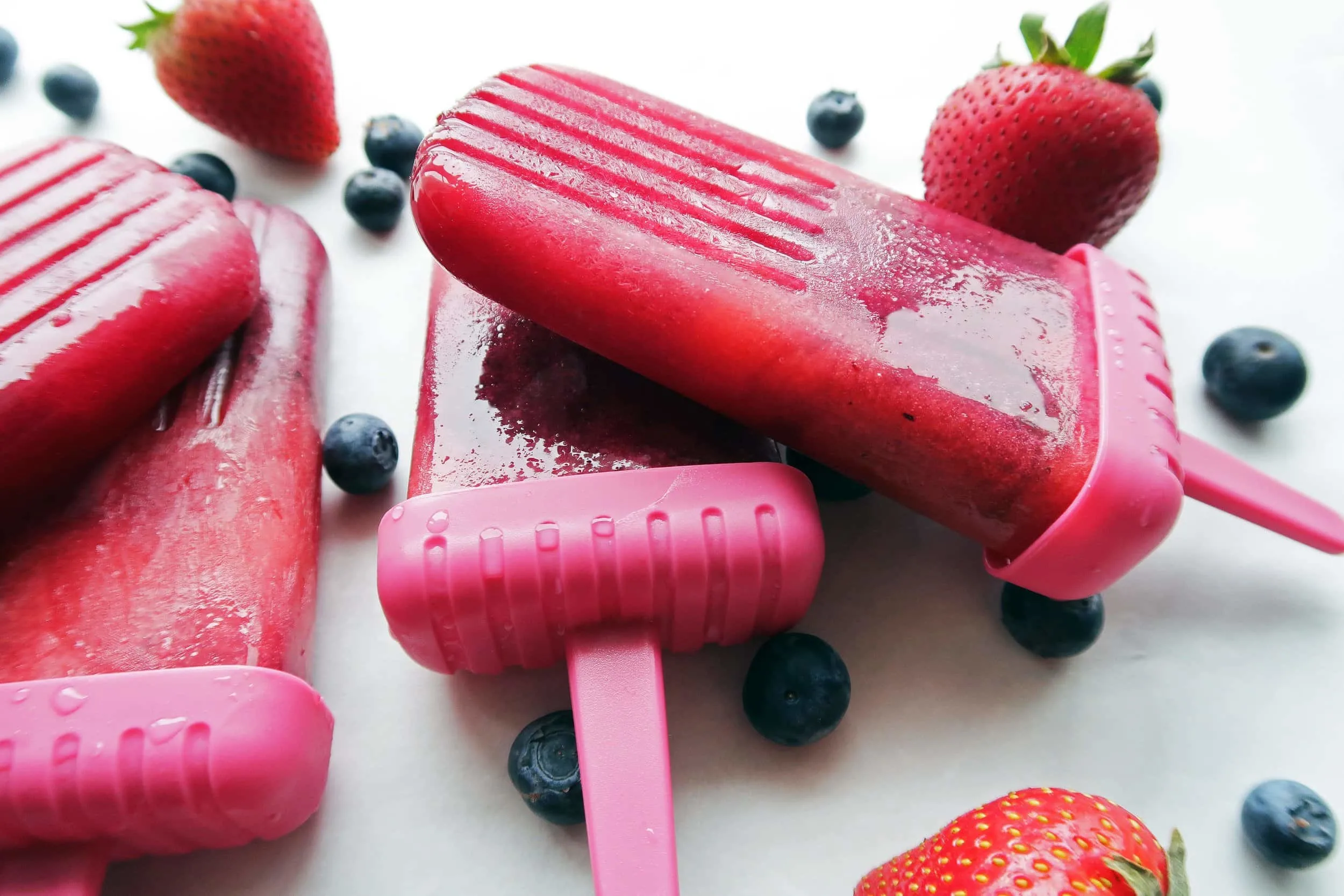 Five Strawberry Blueberry Coconut Water Popsicles with strawberries and blueberries around them.