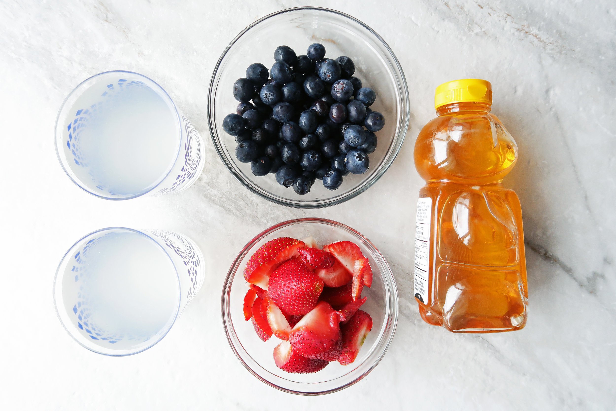 Bowls of strawberries, blueberries, and coconut water next to a bottle of honey.