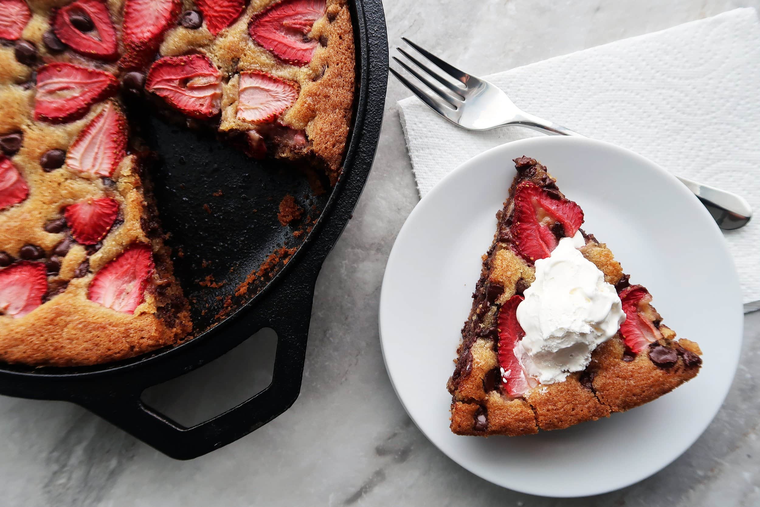 A slice of Strawberry Chocolate Chip Skillet Cookie topped with whipped cream.