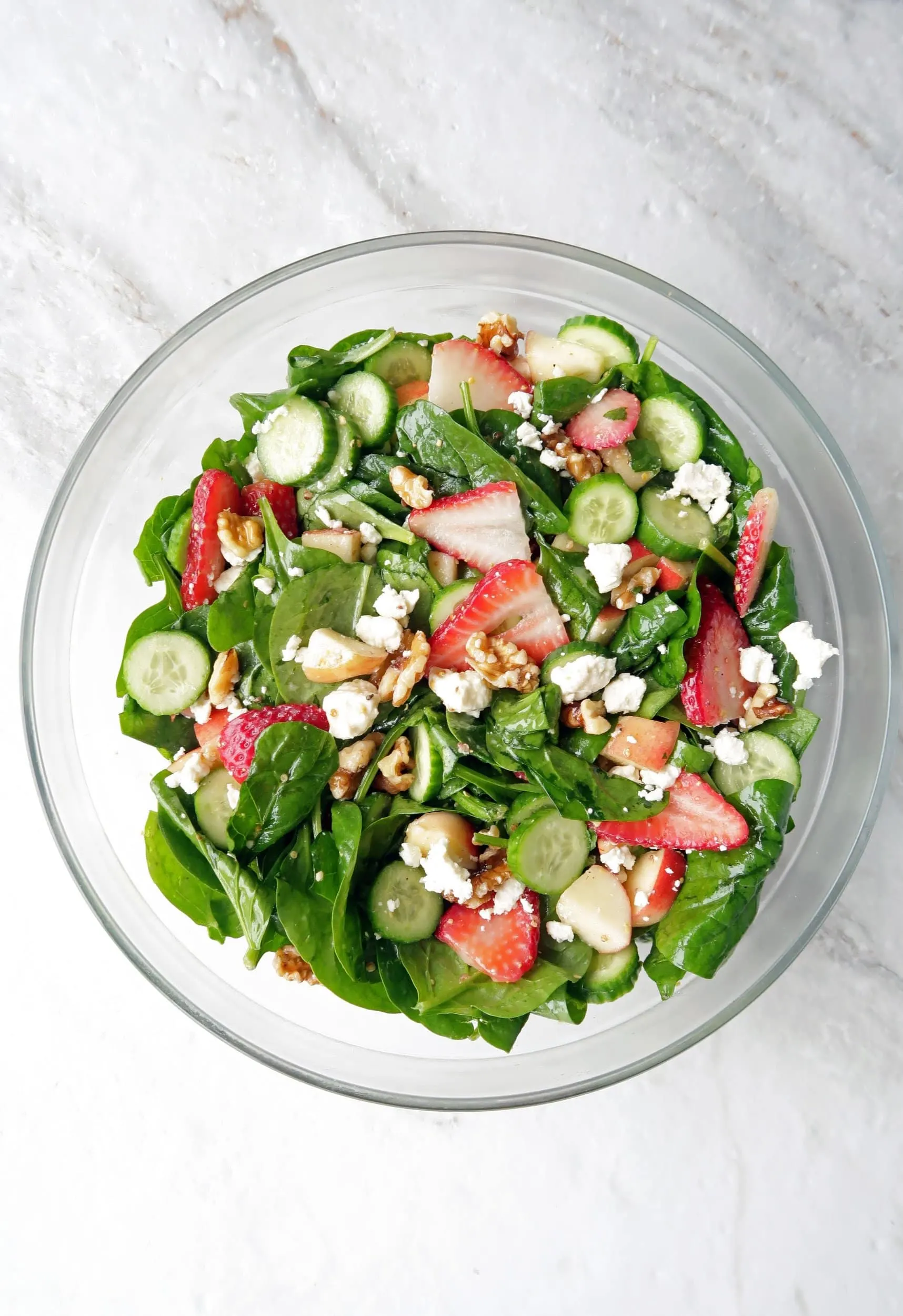 Summer Strawberry Cucumber Spinach Salad that's been tossed with Apple Cider Vinaigrette in a large glass bowl.